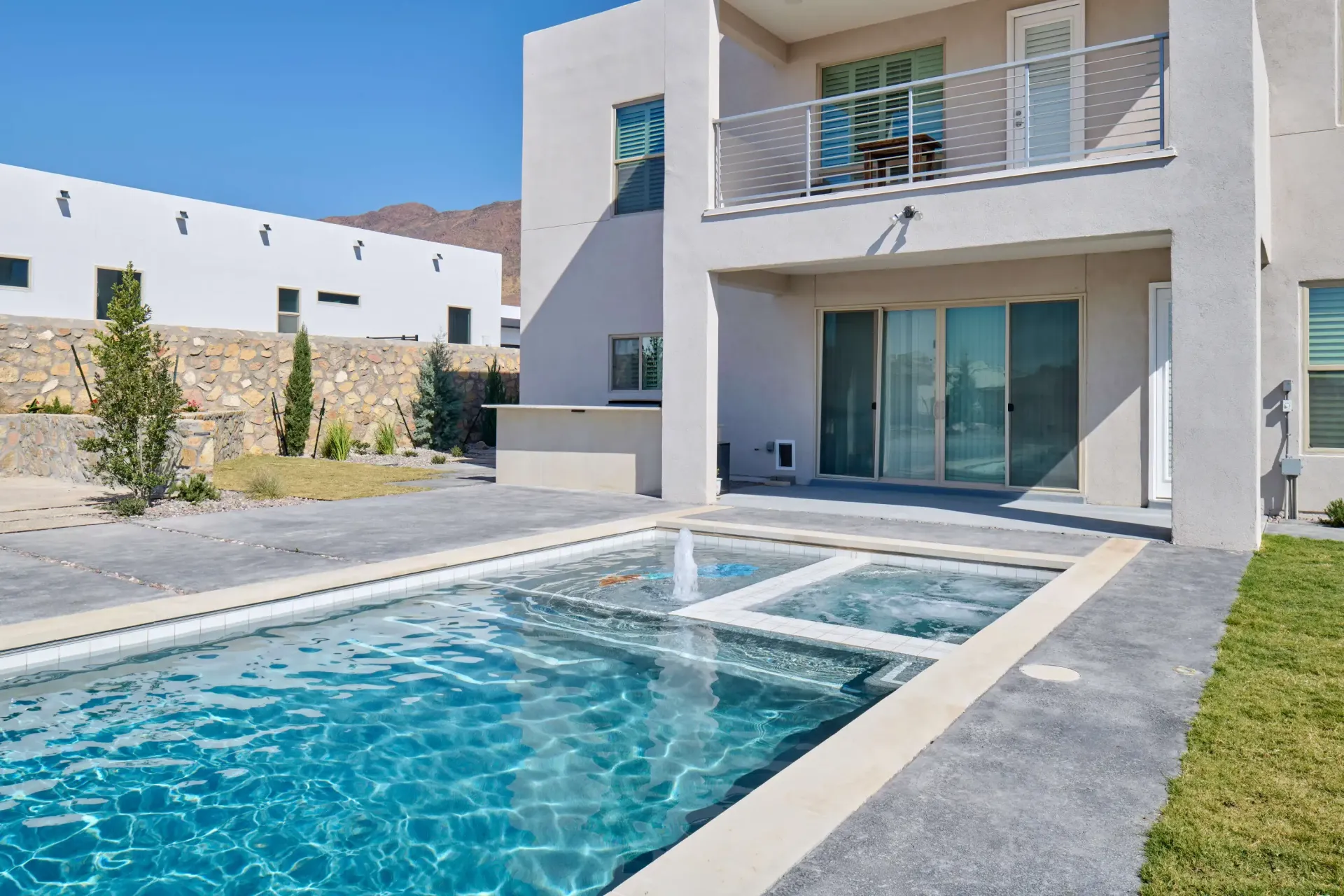 Backyard pool with a connected jacuzzi and a modern house.