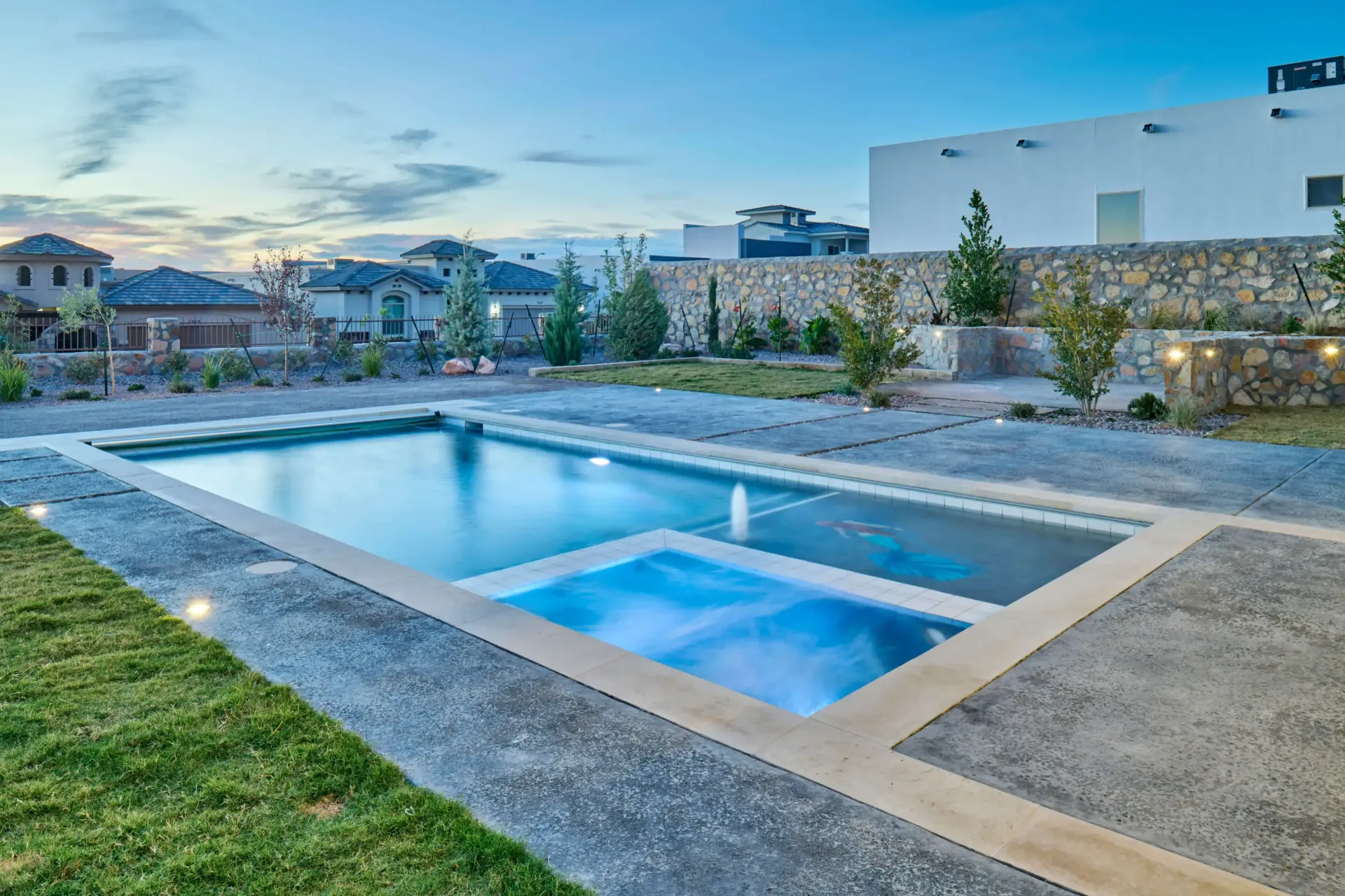 Rectangular pool with spa, concrete surround, and lawn in a residential backyard at dusk.