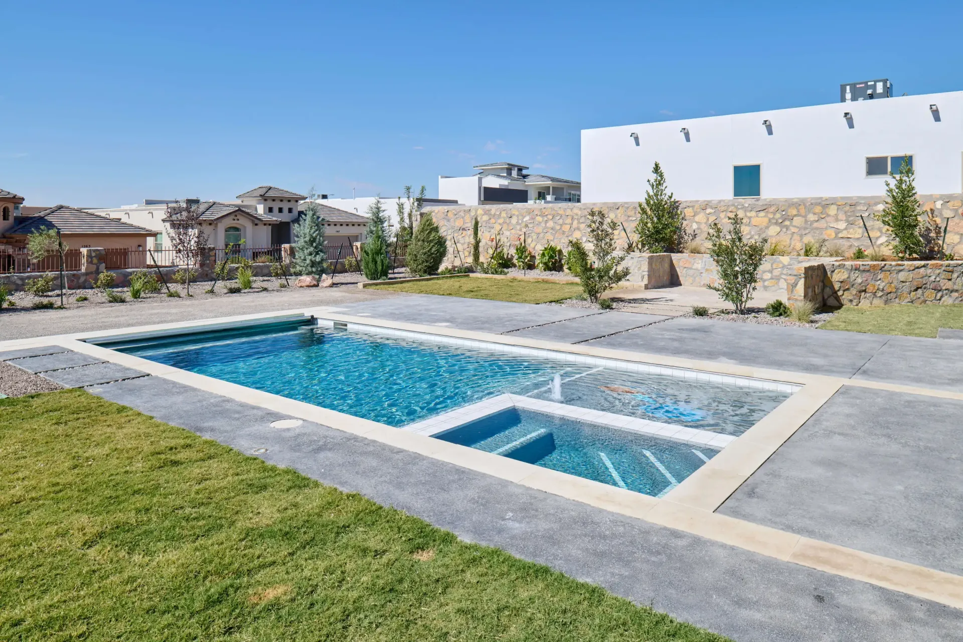 Rectangular pool with turquoise water, surrounded by concrete and grass, in a residential area.