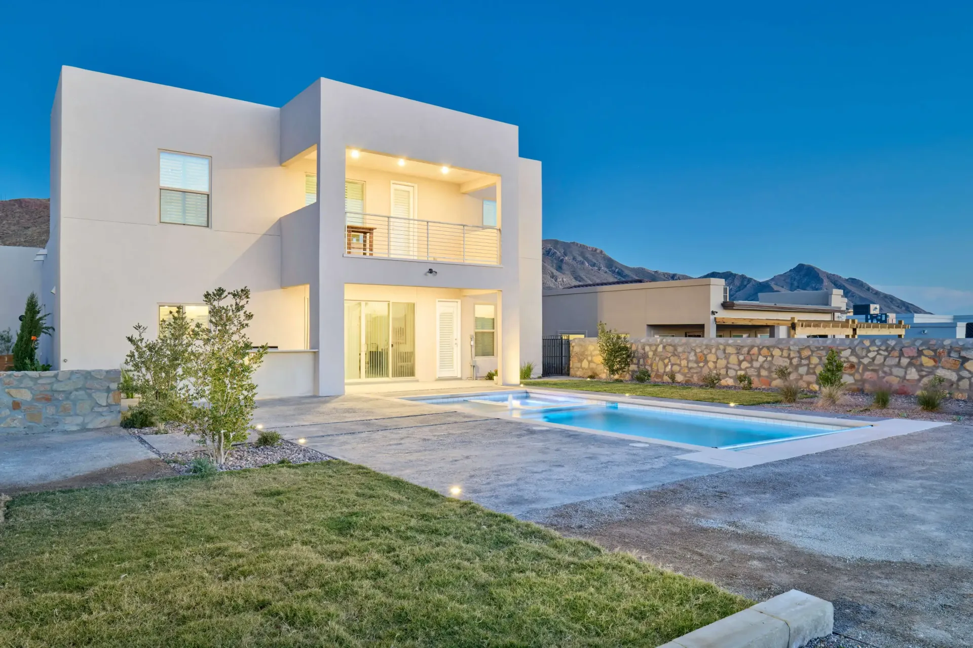 Modern white house with a pool in a desert landscape at dusk.