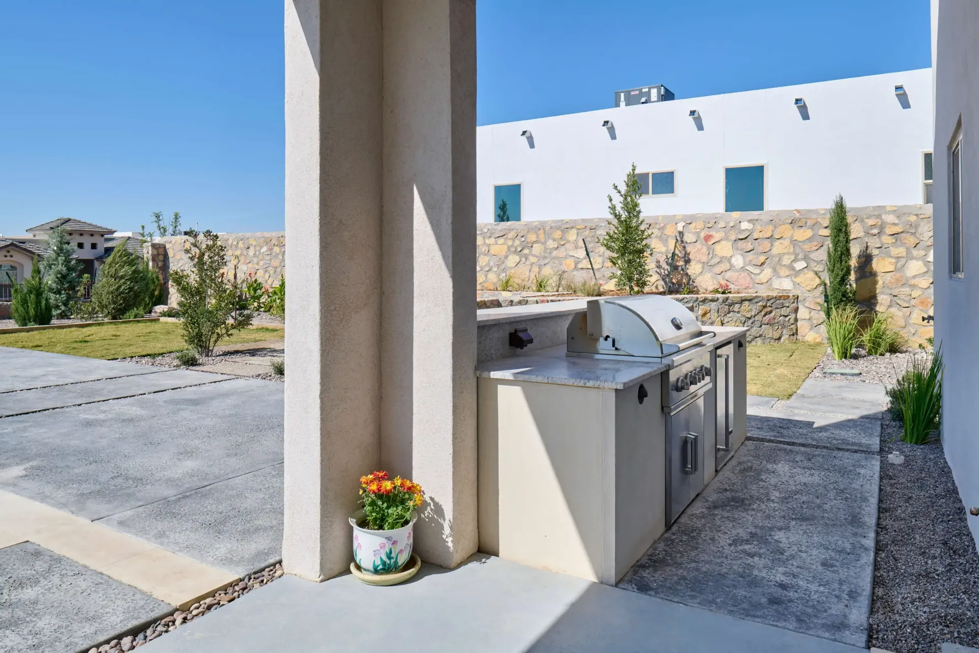 Outdoor kitchen area with built-in grill, concrete patio, and white stucco building in the background.