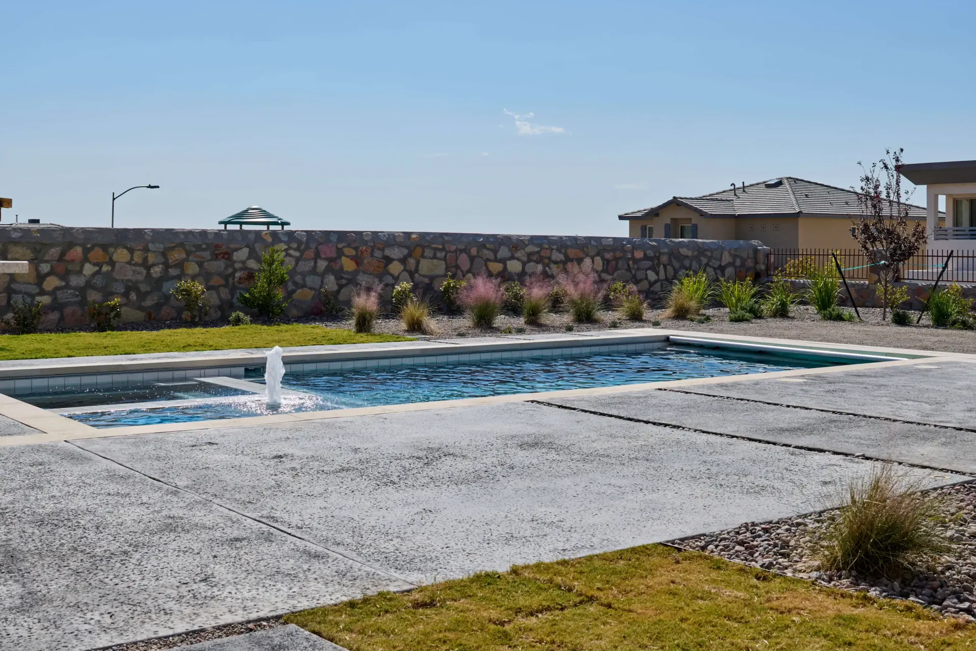 Rectangular pool with fountain, stone wall backdrop, sunny day.