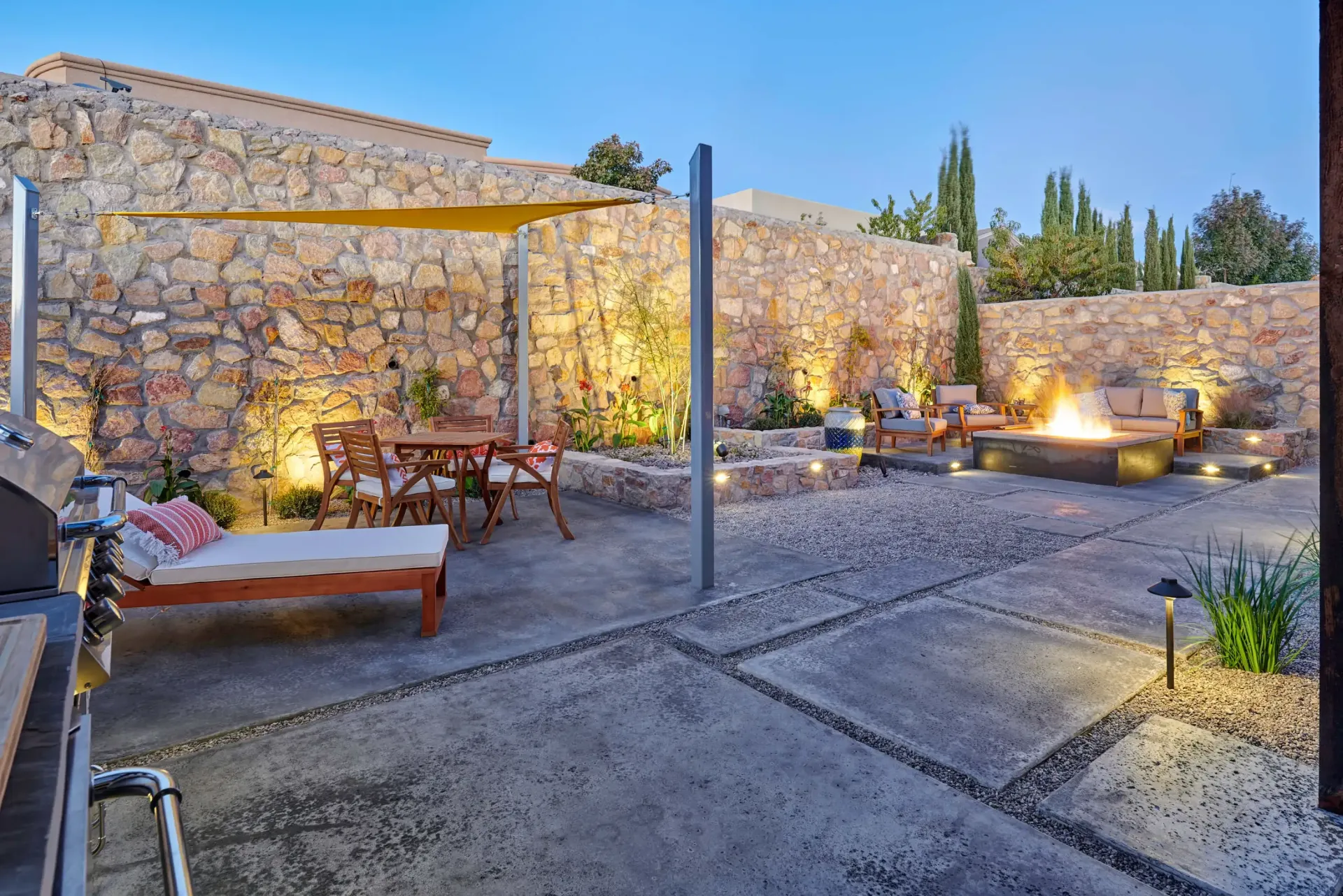 Outdoor patio with stone walls, fire pit, and seating. Lit with warm lights.