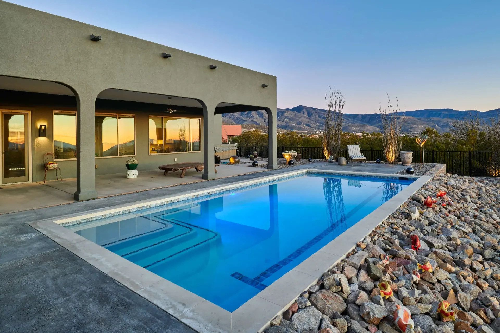 Rectangular pool with blue water next to a house with an arched patio. Mountains visible in the background.