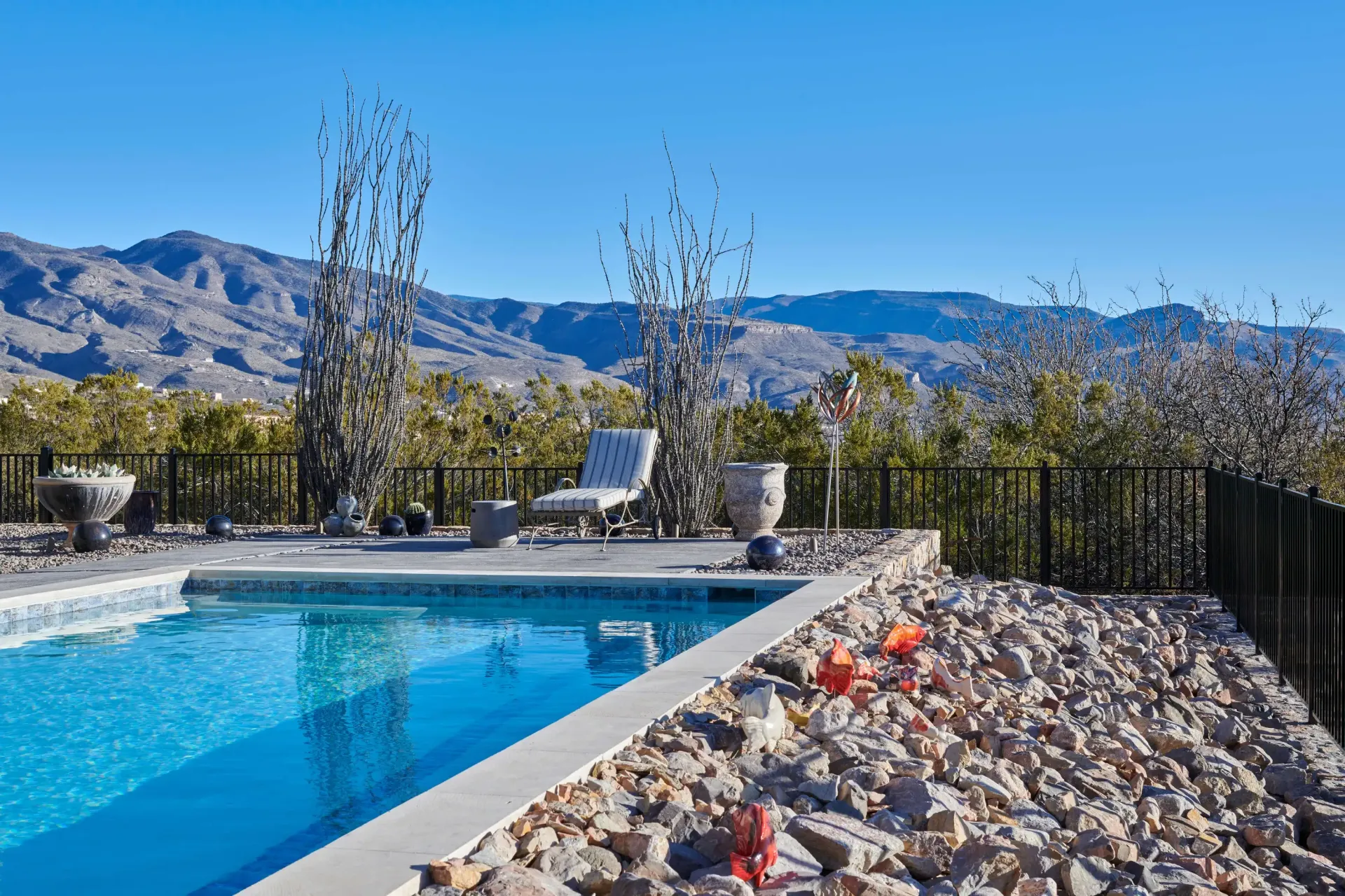 Poolside view with mountains, chair, and decorative rock bed.