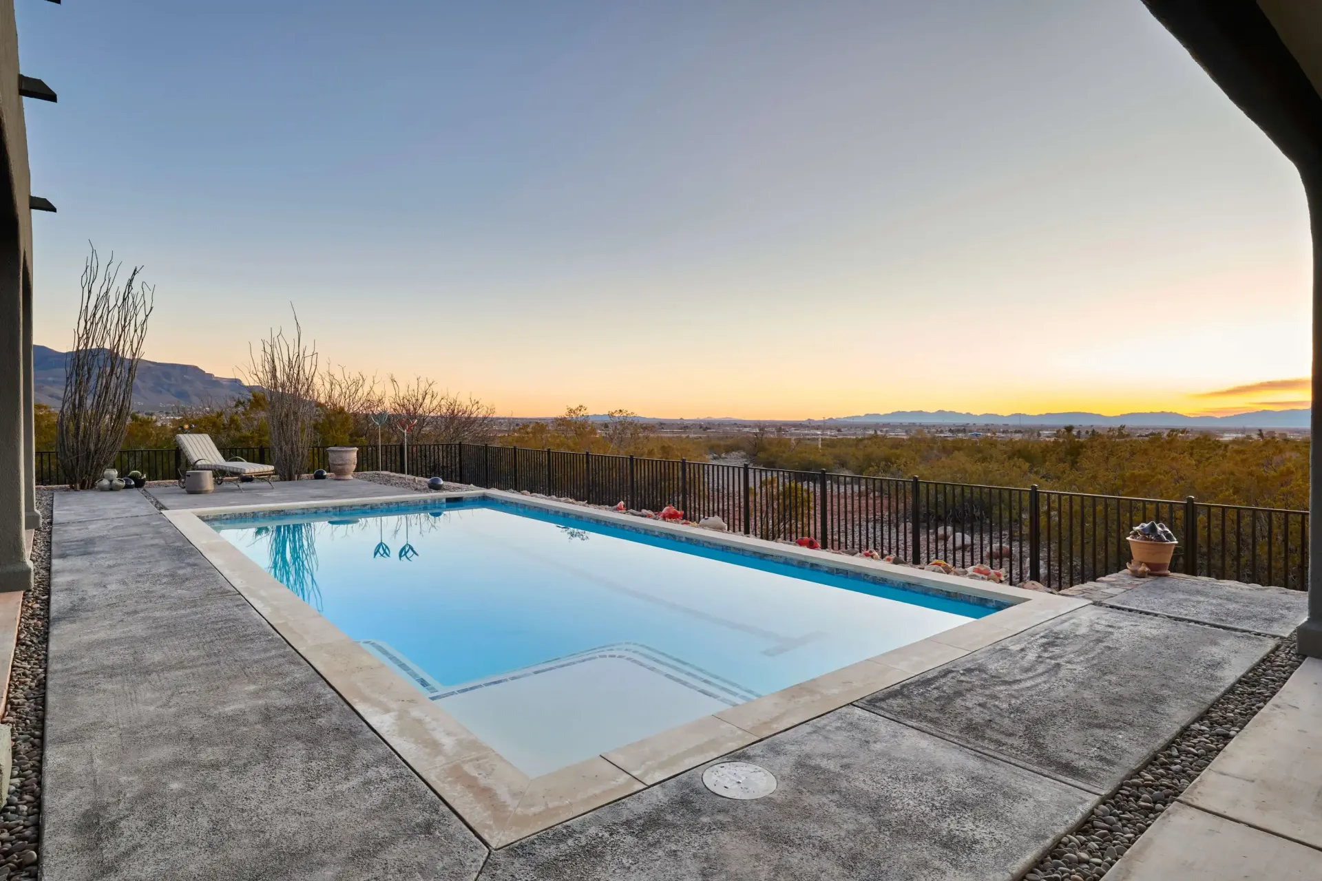 Rectangular pool with clear water, patio, desert landscape, and sunset sky.