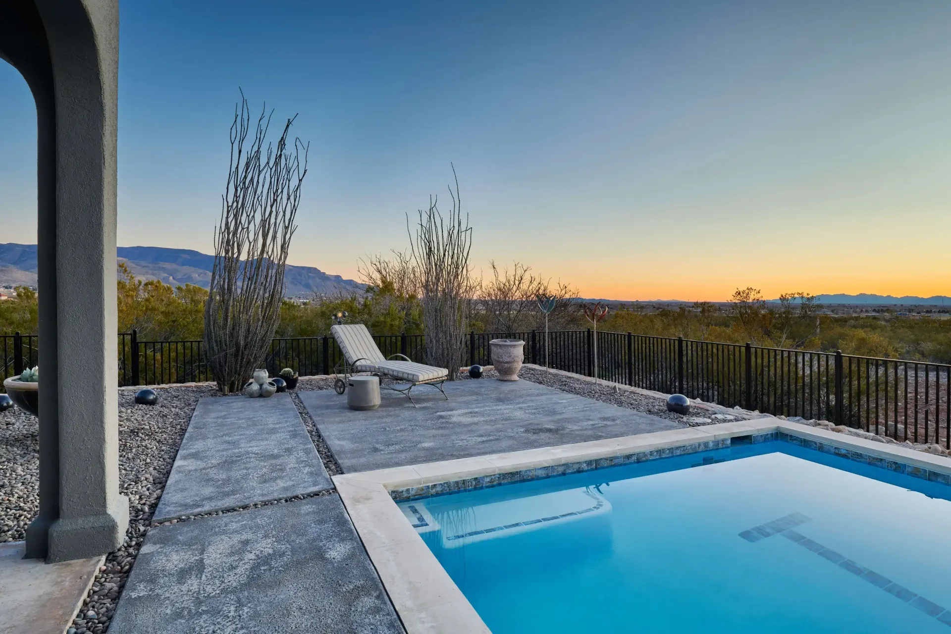 Poolside patio at dusk with a pool, lounge chair, and a view of mountains.
