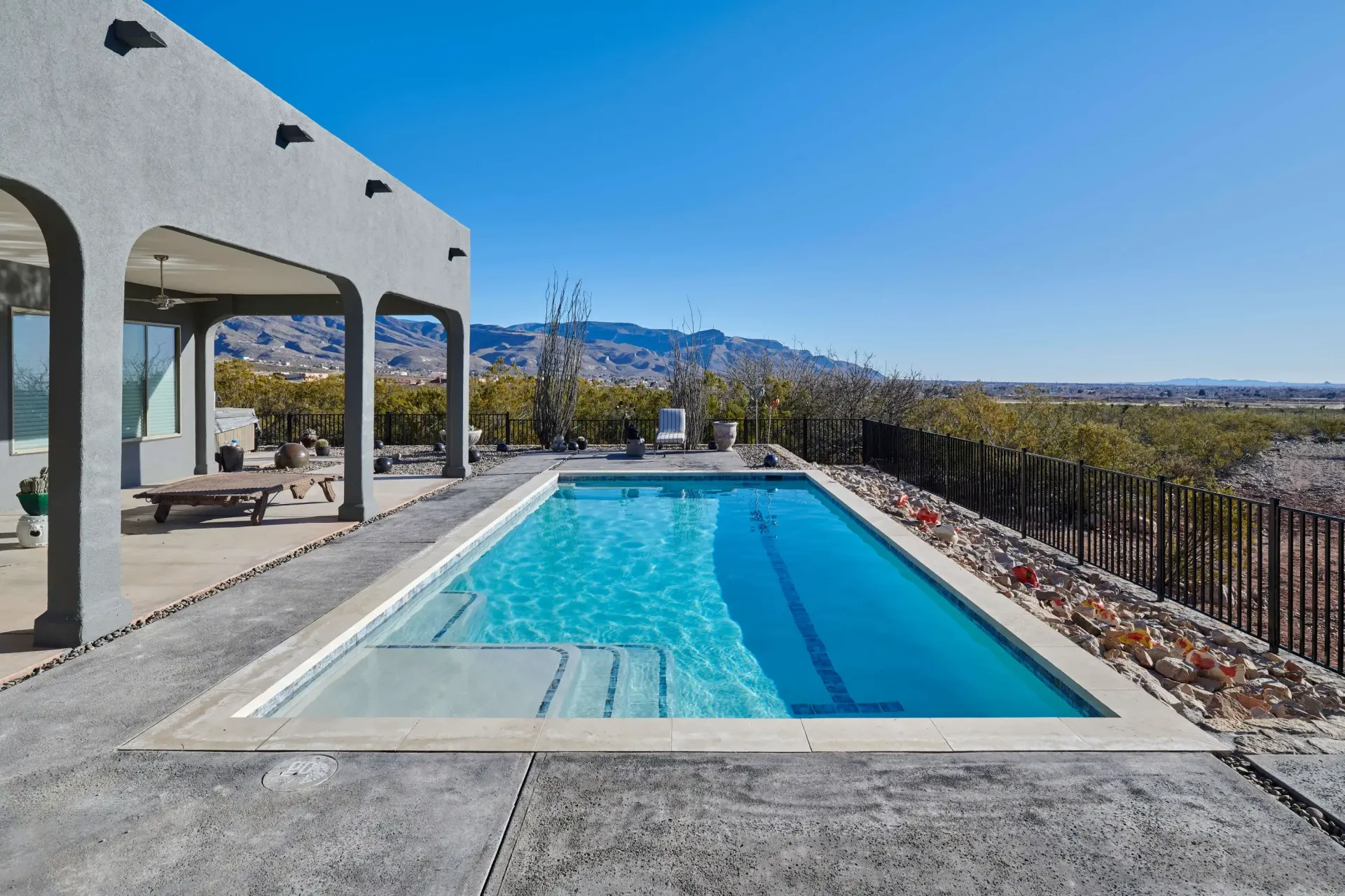 Rectangular pool next to a house with an arched porch, desert landscape in the background.