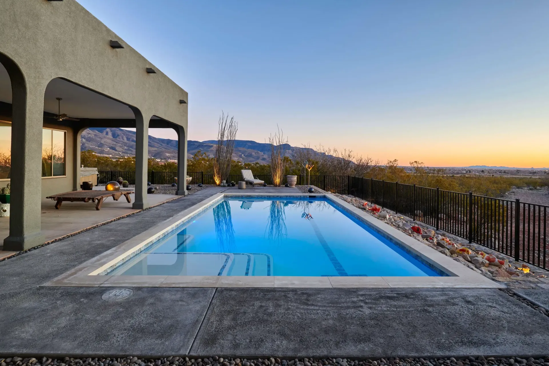 Swimming pool with a view, next to a covered patio. Dusk sky, mountain background.