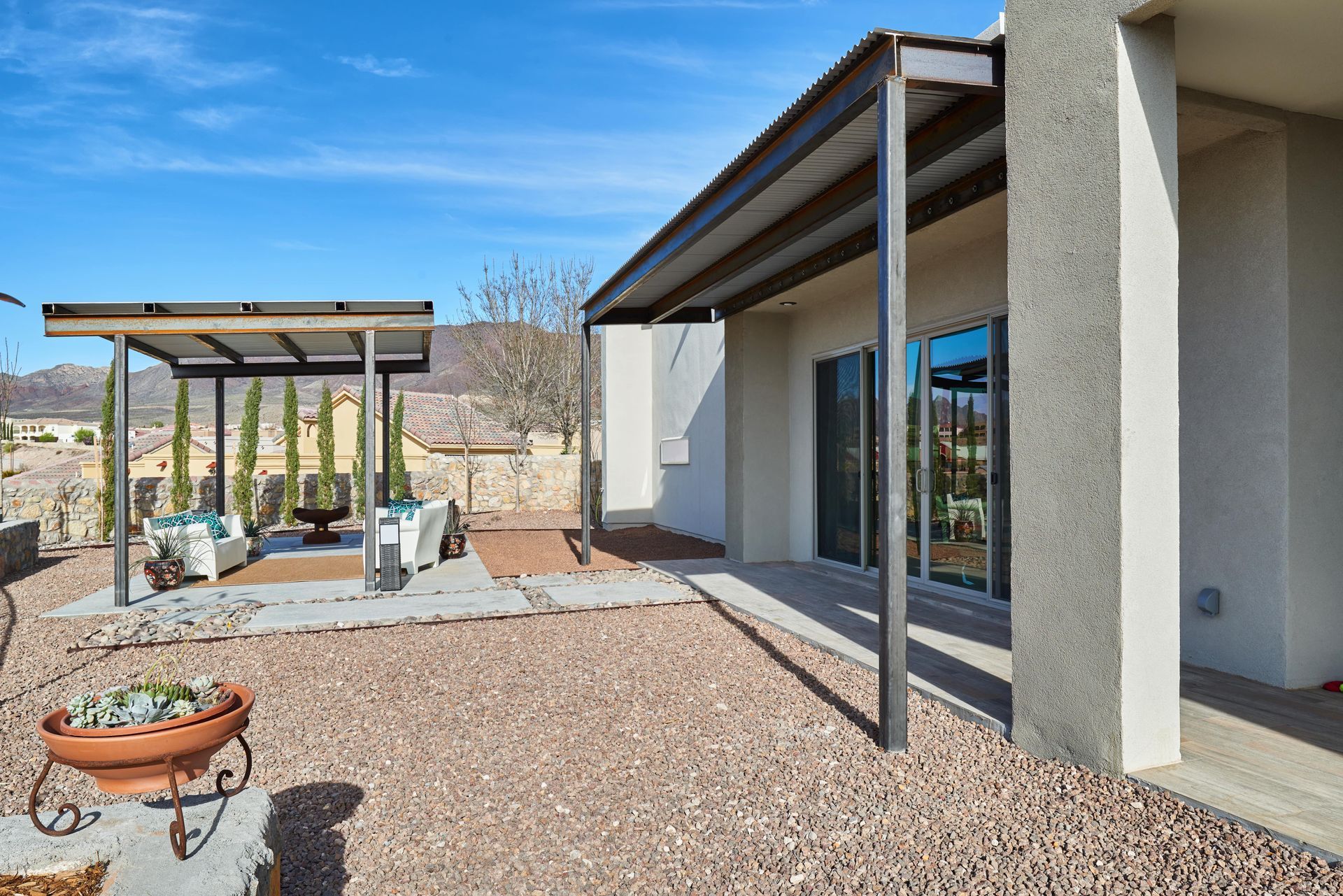 Backyard with patio, covered seating areas, and desert landscaping under a blue sky.