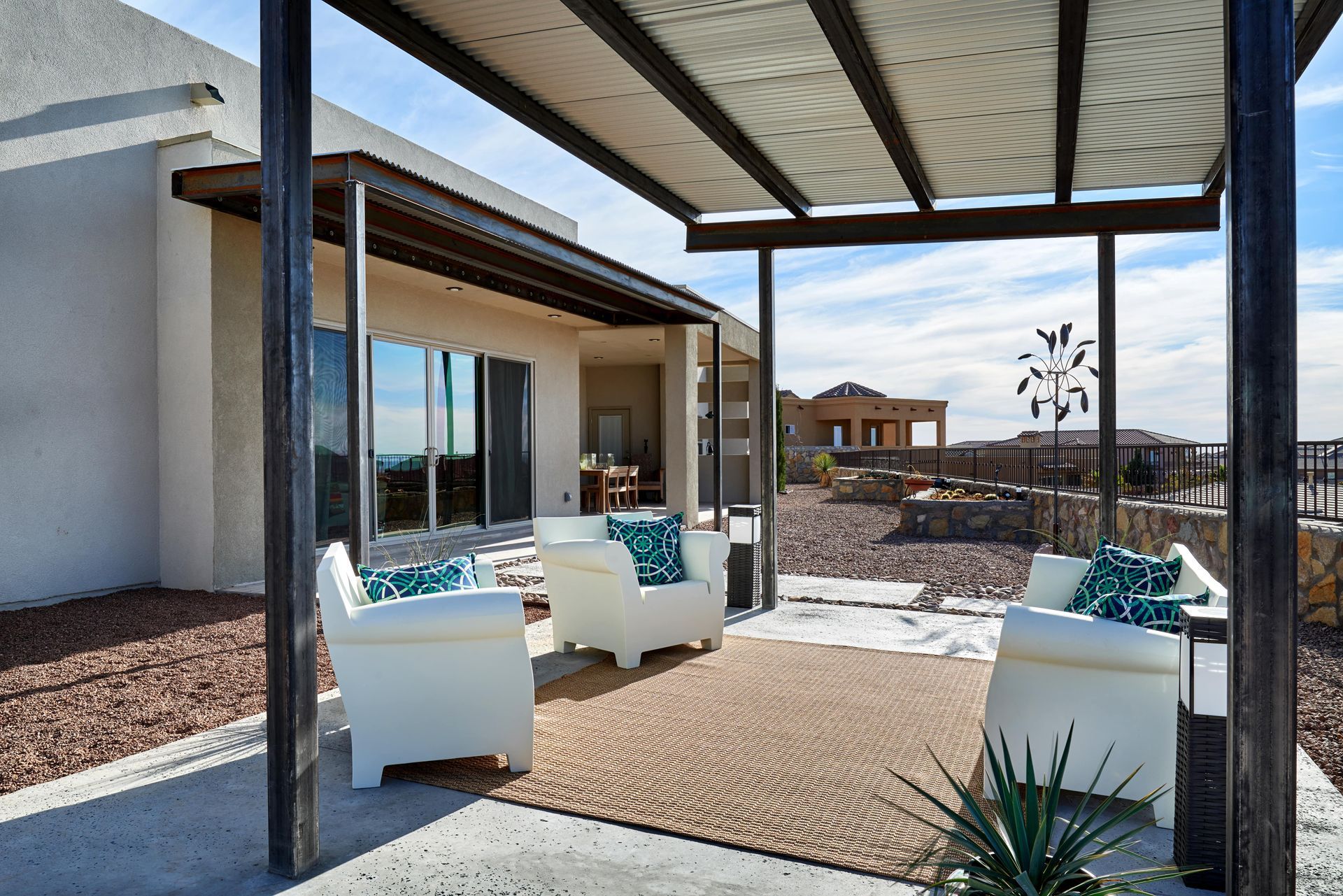 Outdoor seating area with white chairs, rug, and pergola, overlooking a landscape with houses.