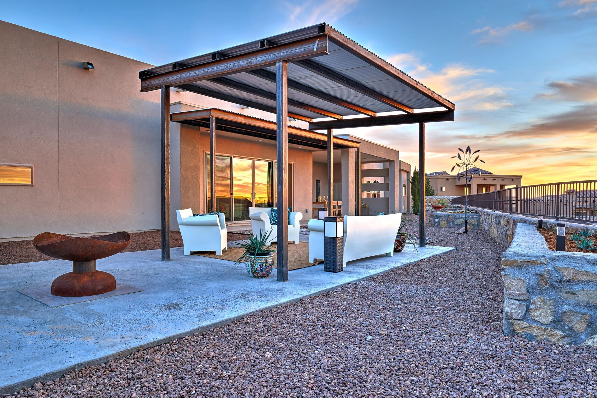 Patio with seating under a shaded pergola, next to a modern building at sunset.