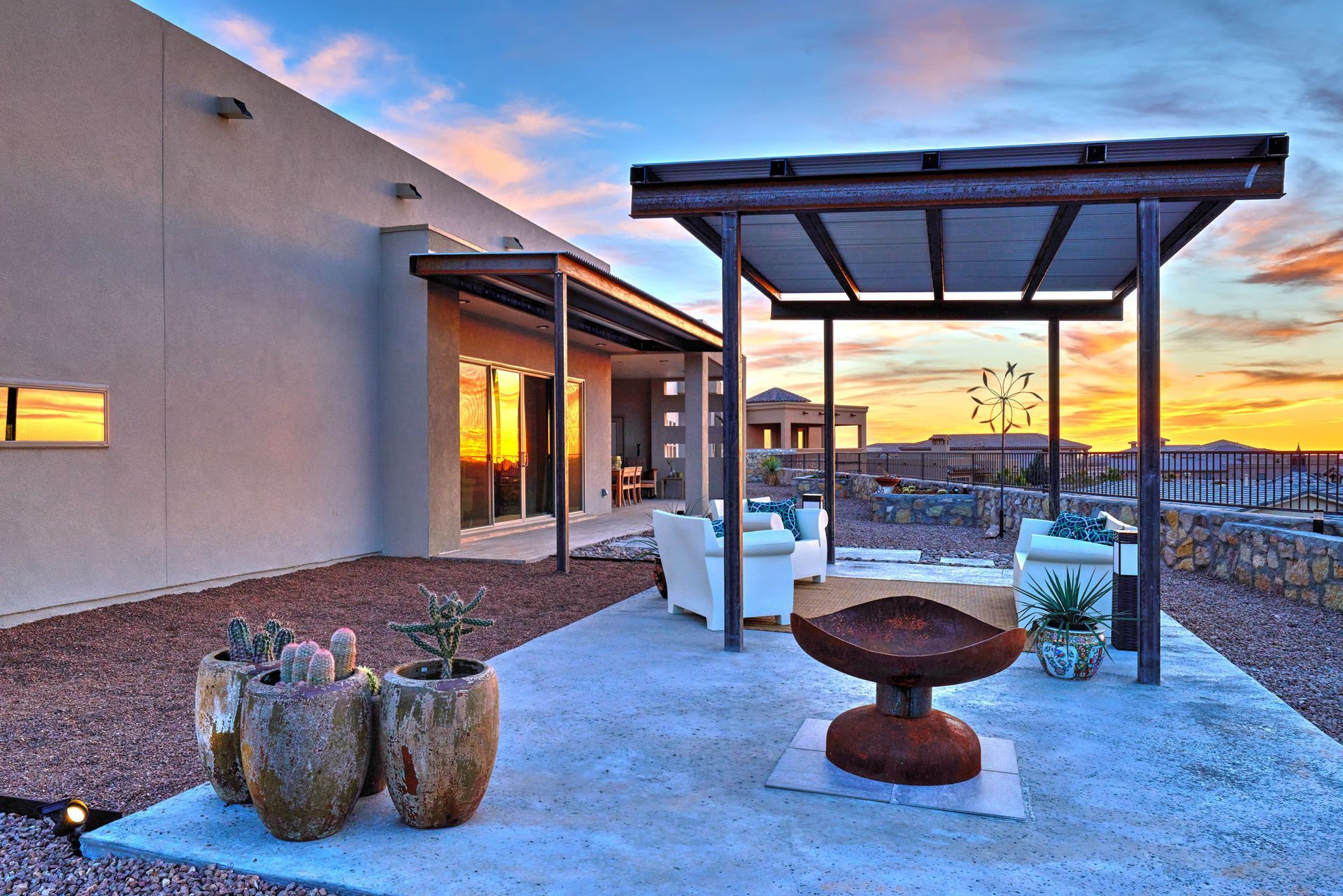 Patio with seating, fire pit, potted plants, and pergola. Sunset sky.