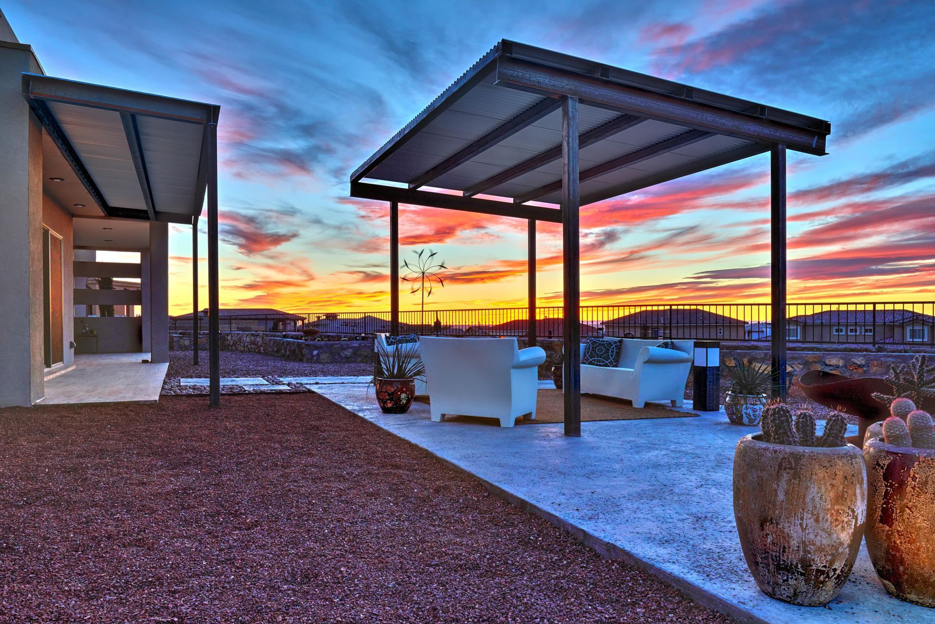 Patio with pergola, white furniture, potted plants, and colorful sunset sky.