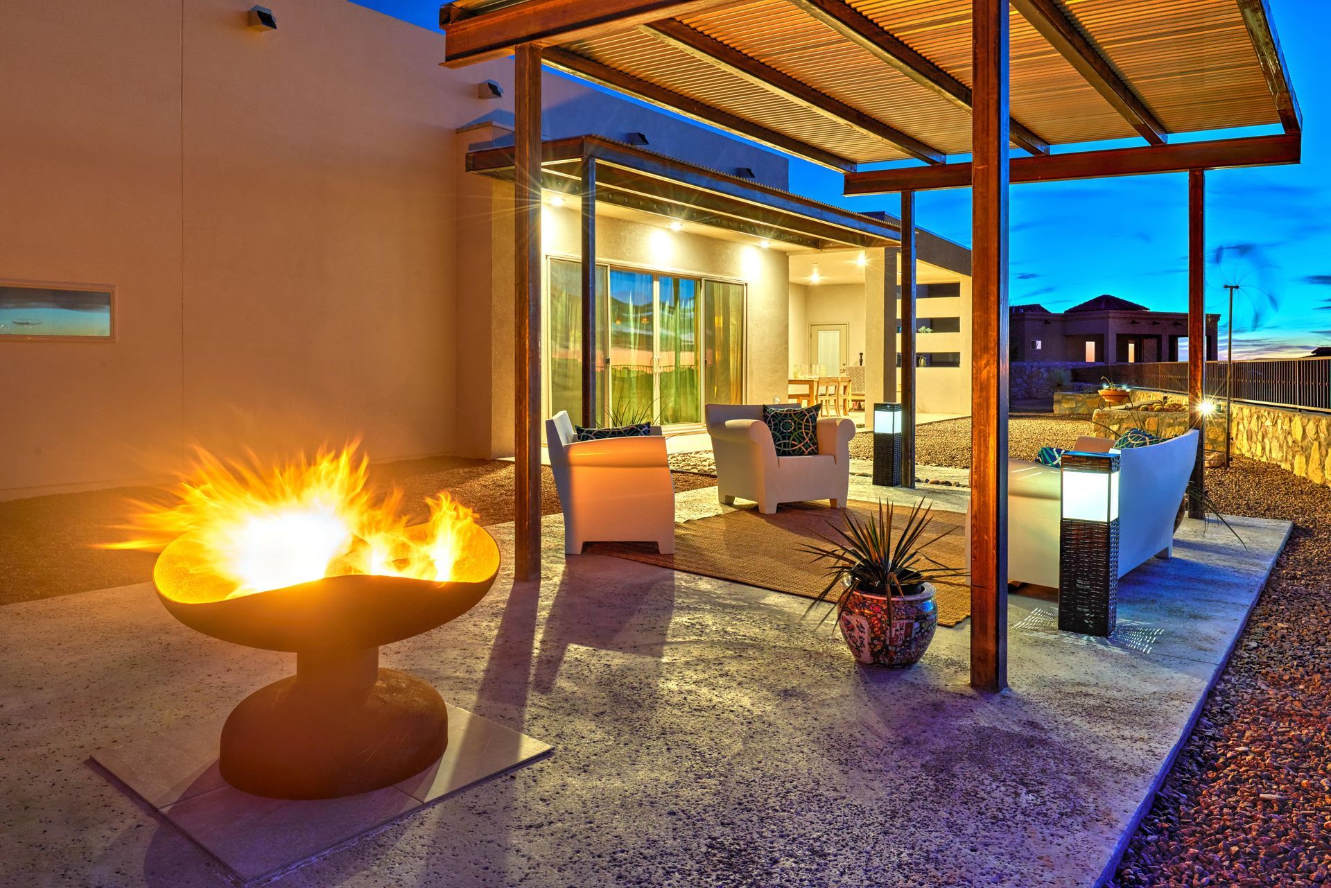 Outdoor patio with fire pit, seating, and pergola at dusk.