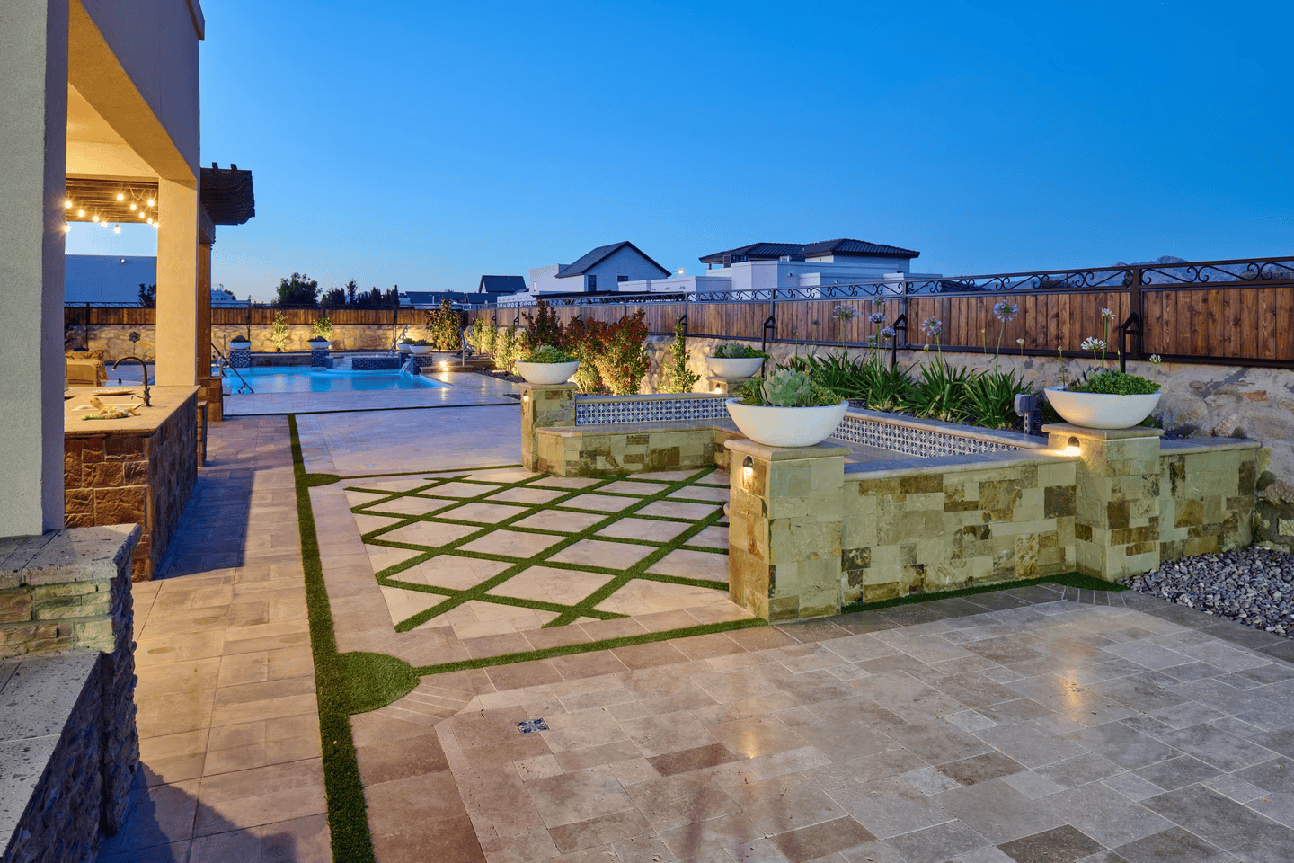 Outdoor patio with stone walls, planters, and a swimming pool at dusk.