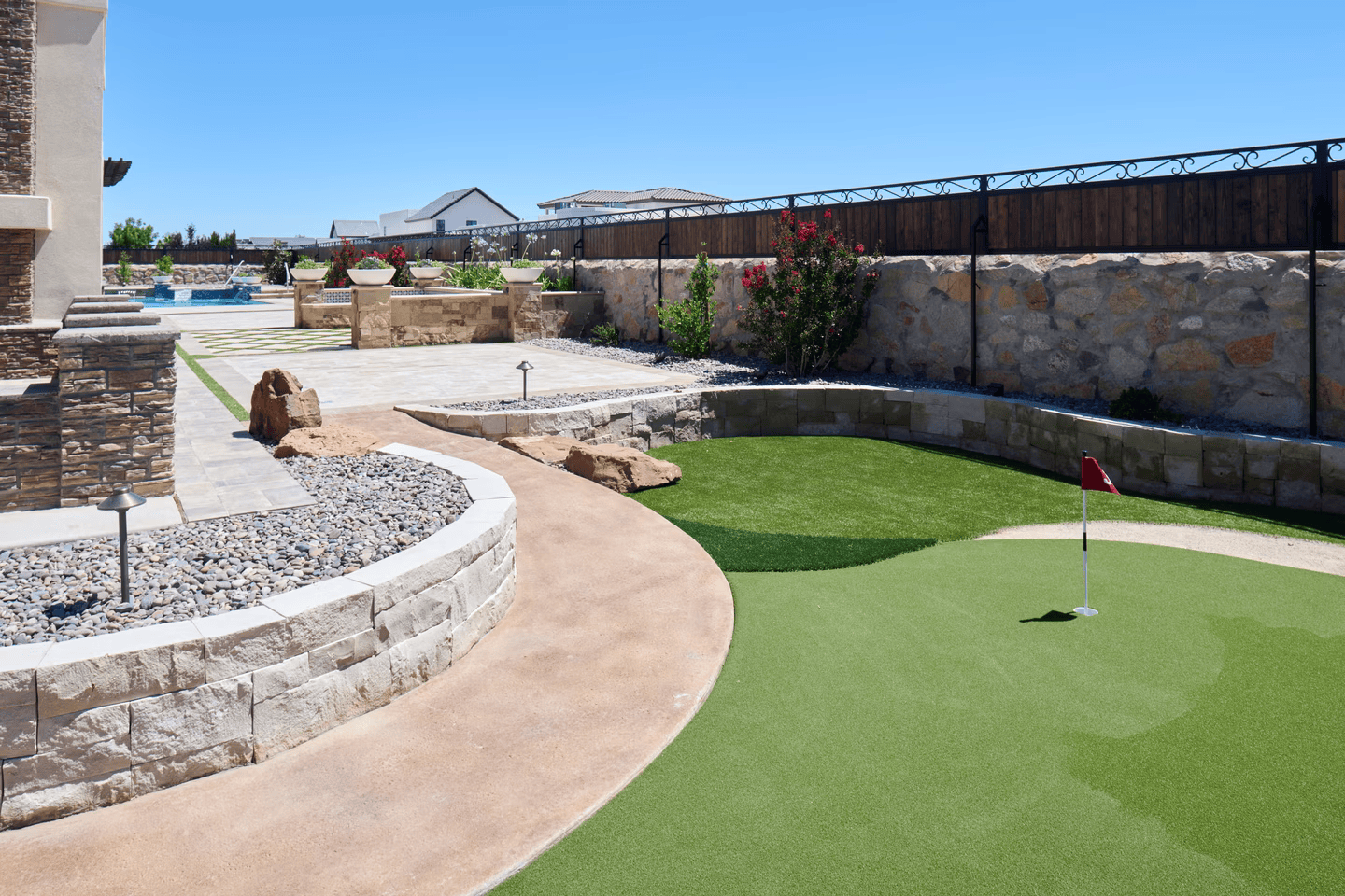 Backyard with putting green, stone walls, pathway, and landscape with clear blue sky.