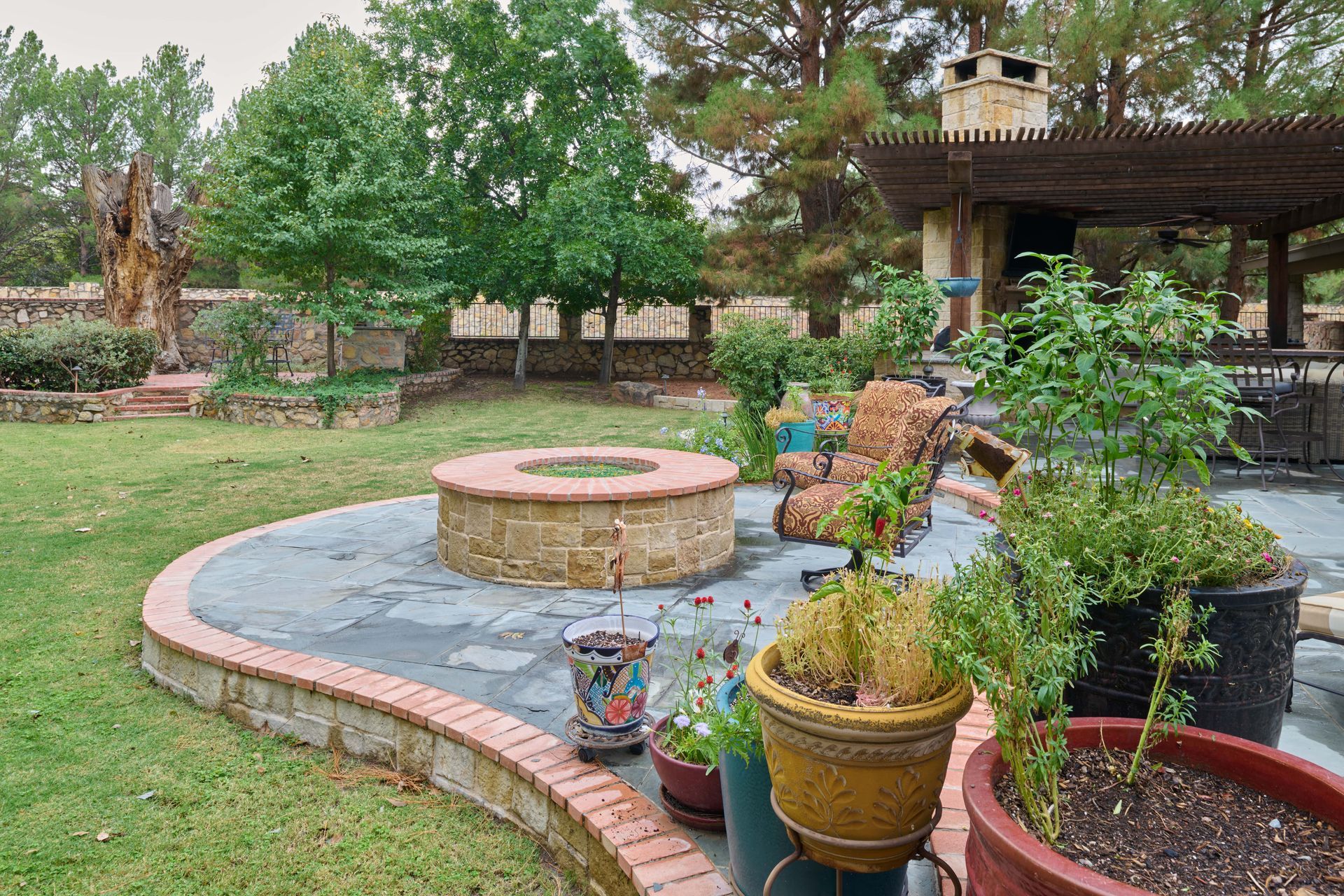 Backyard patio with fire pit, seating, plants, and covered structure.