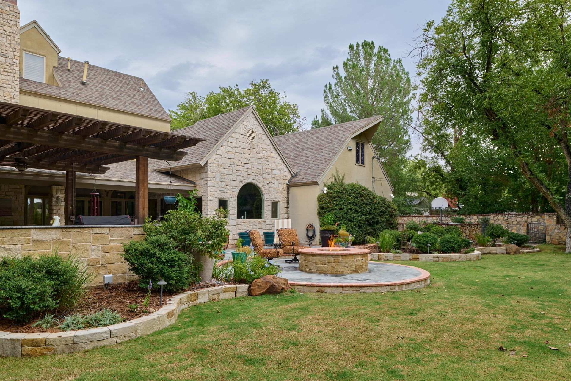 Backyard with stone patio, fire pit, and house with beige brick.