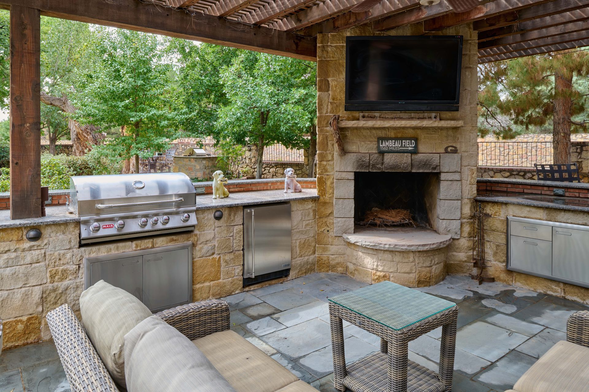 Outdoor patio with grill, fireplace, seating, and TV under a pergola.