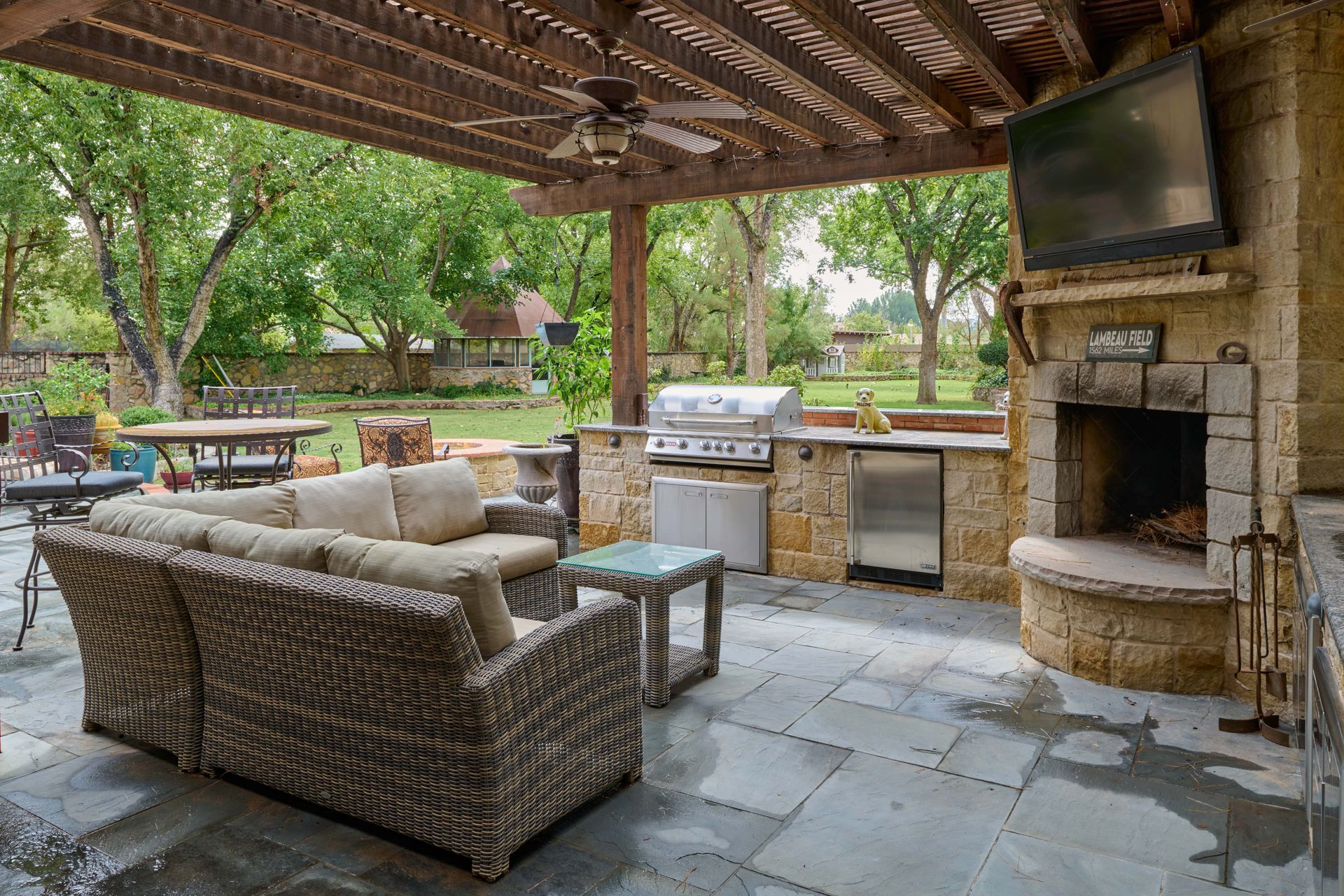 Outdoor patio with stone fireplace, grill, and seating under a wooden pergola.