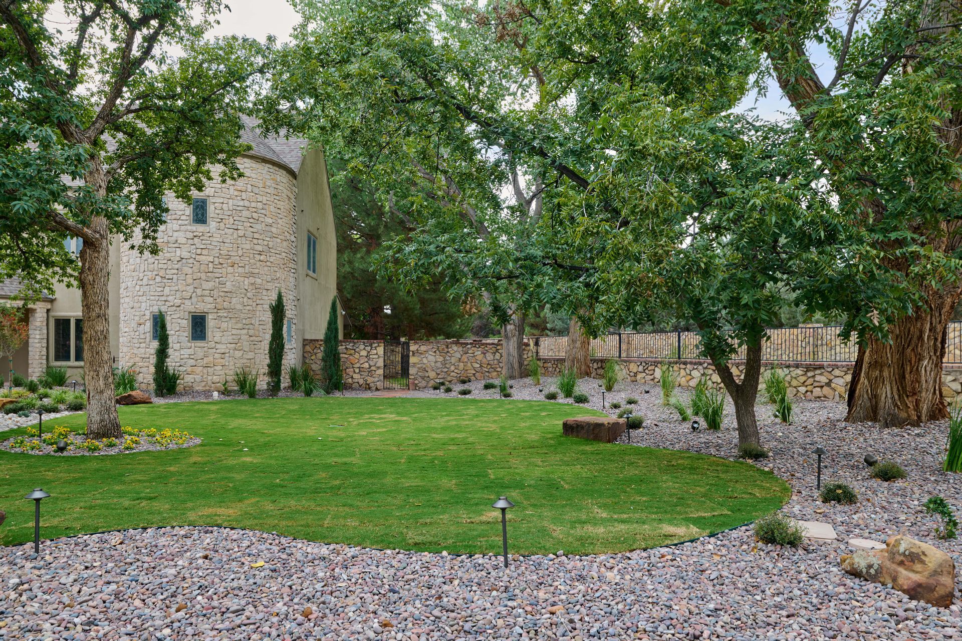 Lush green lawn with trees and stone building in the background, surrounded by gravel and garden beds.