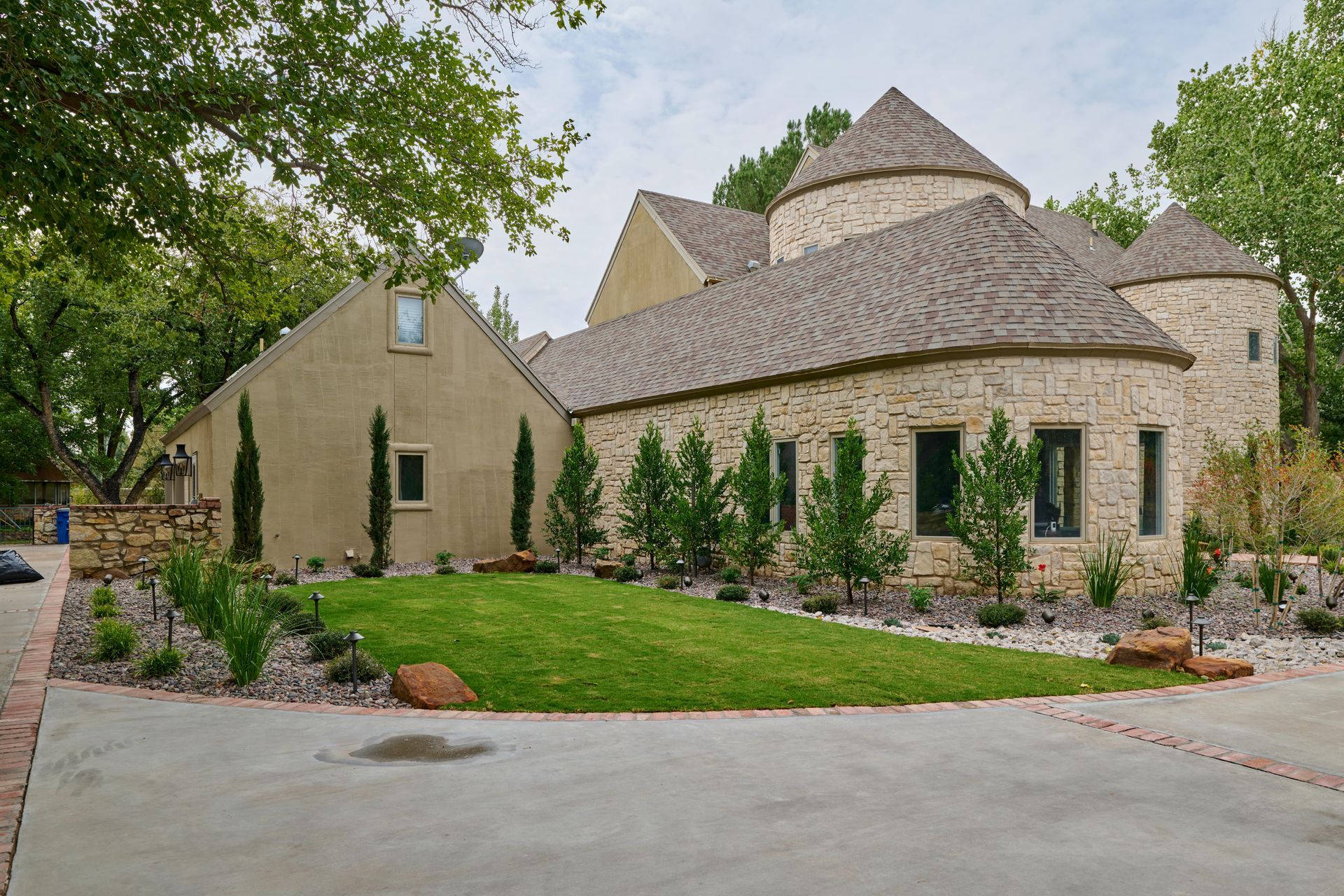 Stone house with rounded towers, green lawn, trees, and blue sky.