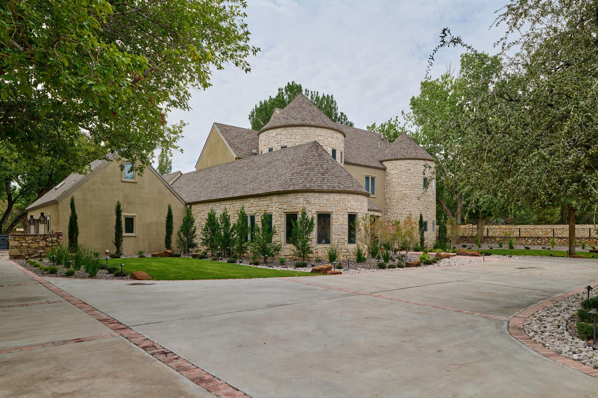 Stone house with circular turrets, gravel driveway, and surrounding trees.
