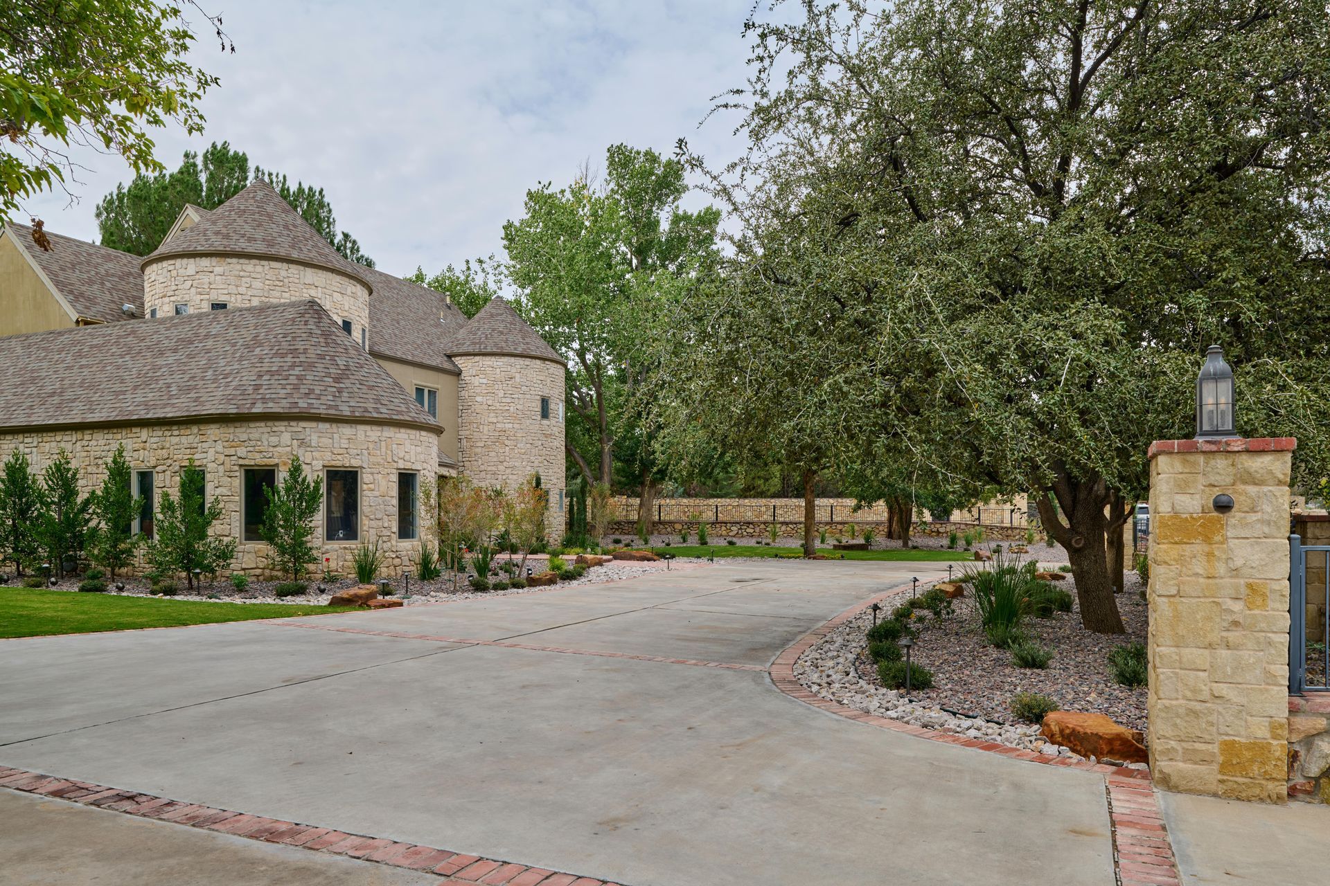 Stone castle with turret, long concrete driveway, and lush landscaping.