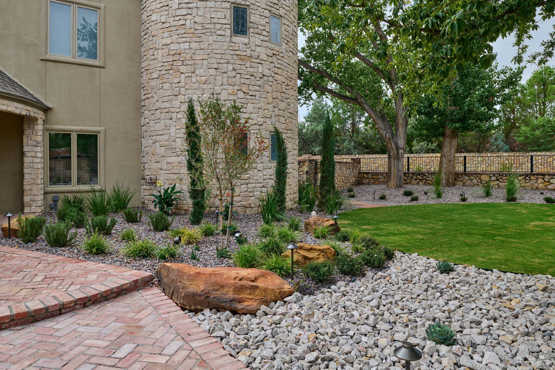 Landscaped front yard with rock and brick pathways, plants, and a stone tower.