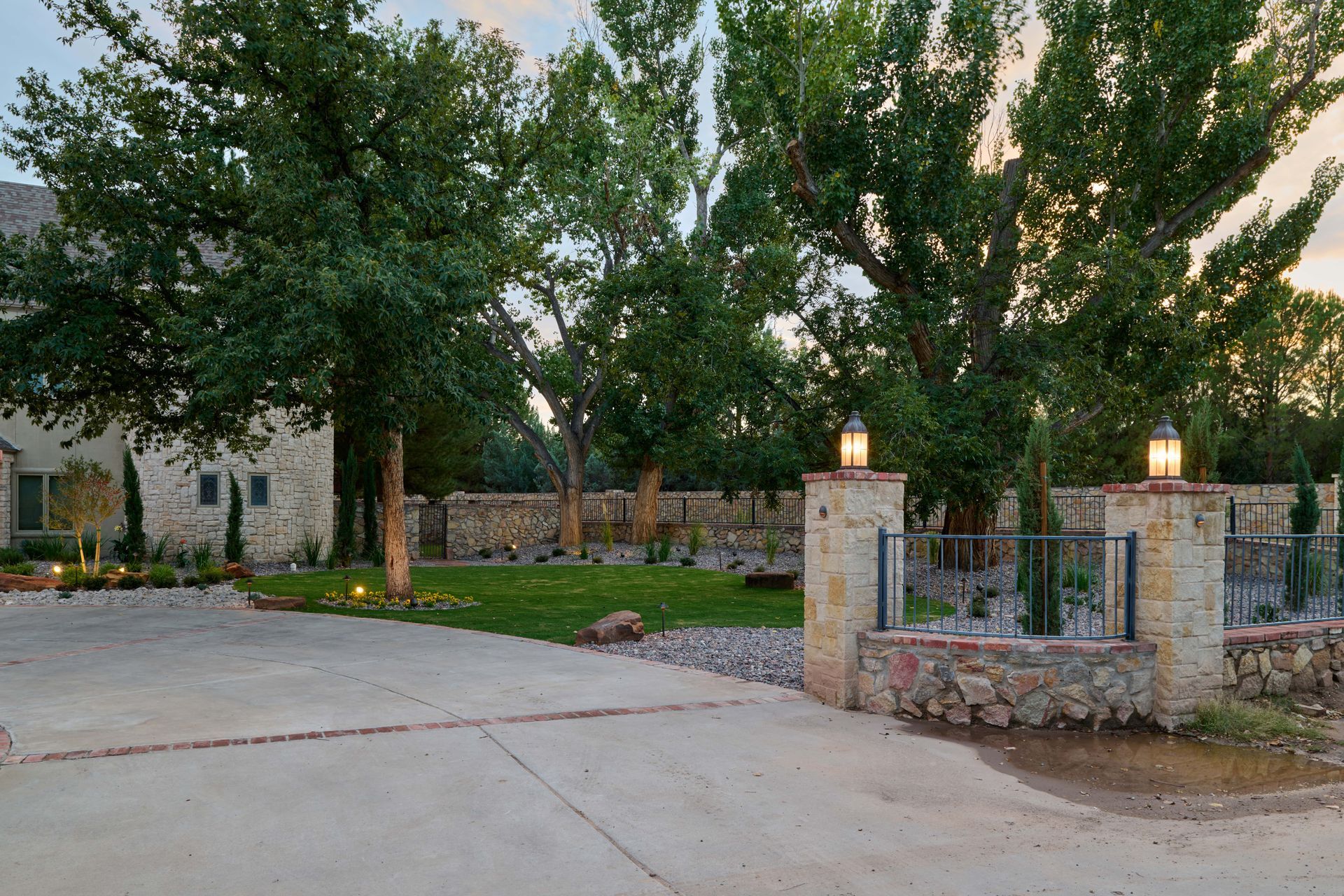Stone entrance to a house with trees and a green lawn, illuminated by lanterns.