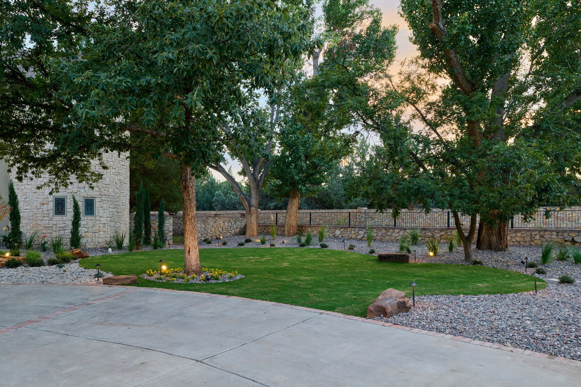 Lush green lawn with trees, stone wall and building exterior, on a gravel driveway.
