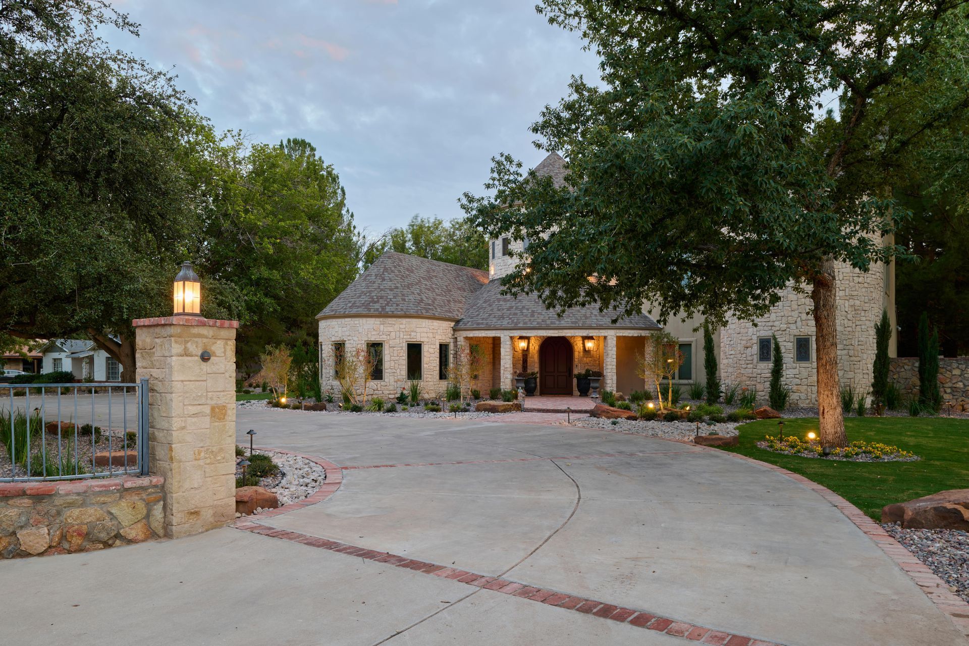 Stone house with circular driveway, lit entryway, and surrounding trees.