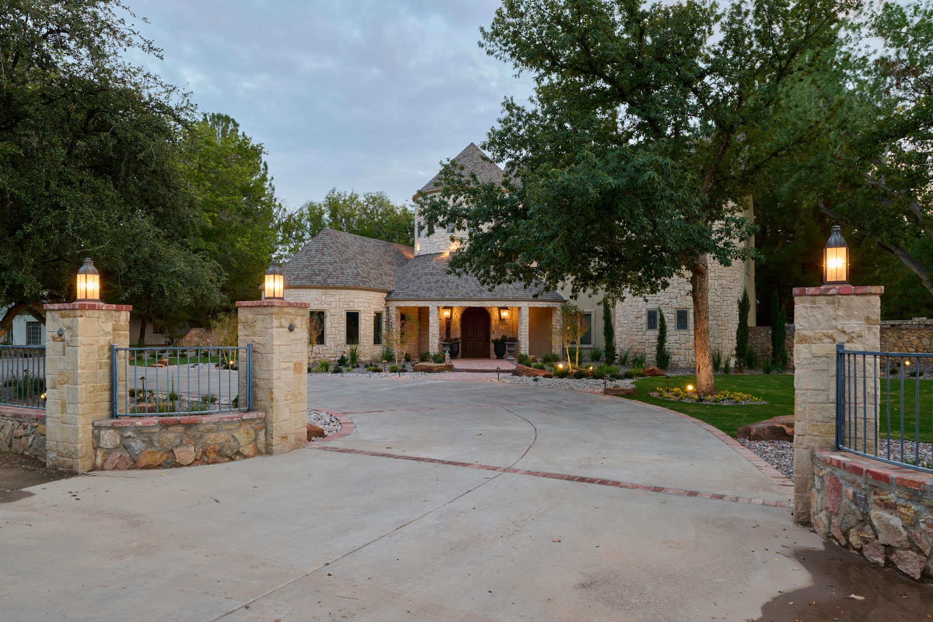 Stone house with long driveway, lanterns, and large trees.