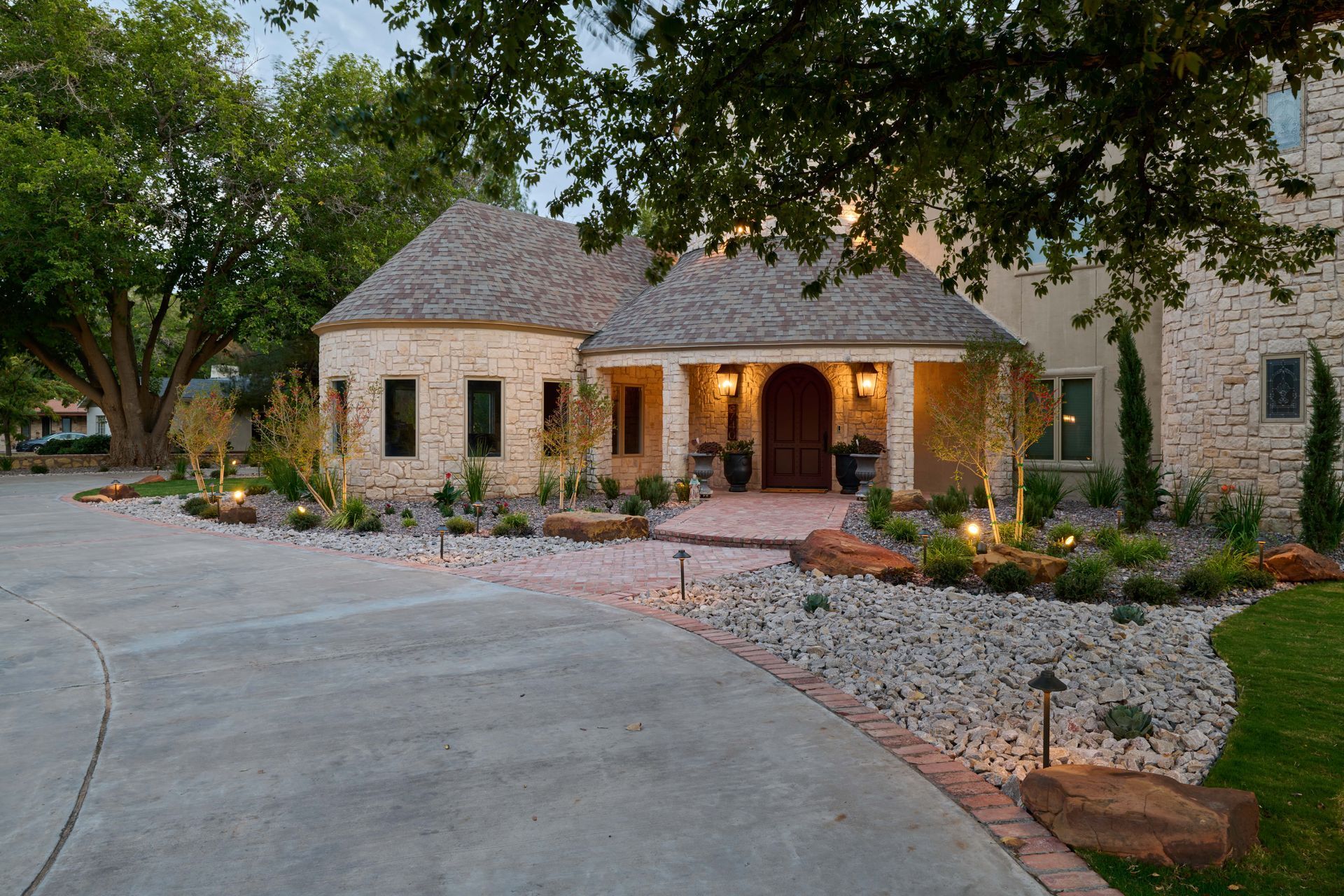 Stone house with a circular turret, arched entry, and landscaped driveway.