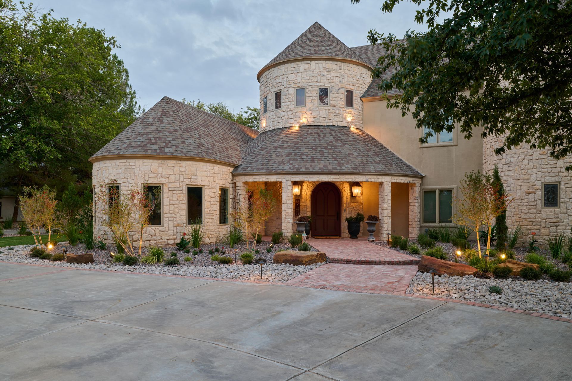 Stone house with round towers, arched entryway, brick path, and landscaped yard.