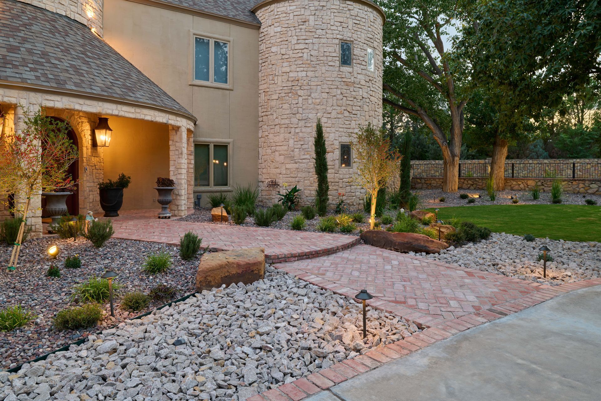 Stone house exterior with lit entryway, brick path, and landscaped yard.