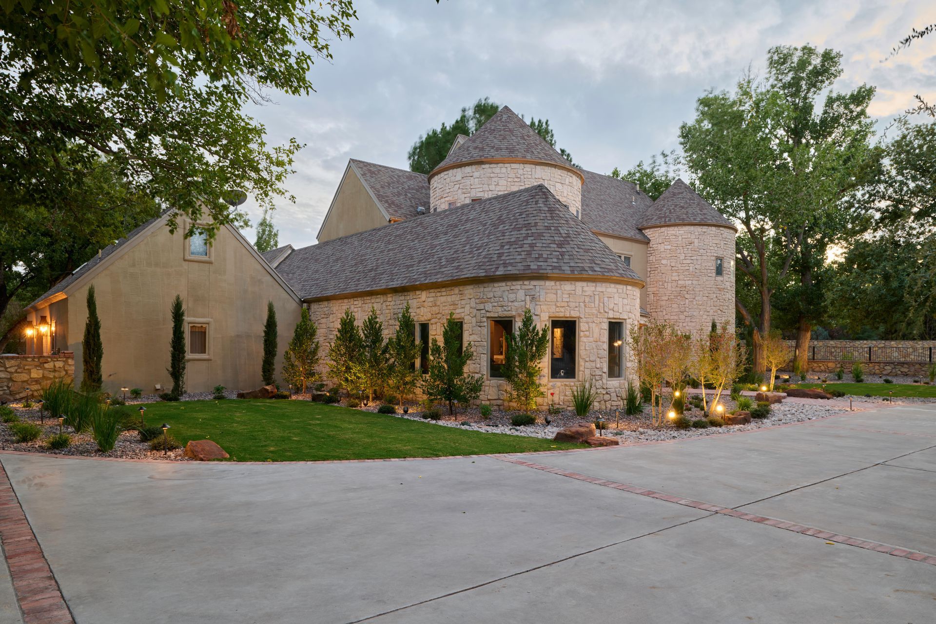 Stone home with circular turret, long driveway, and well-lit landscaping.