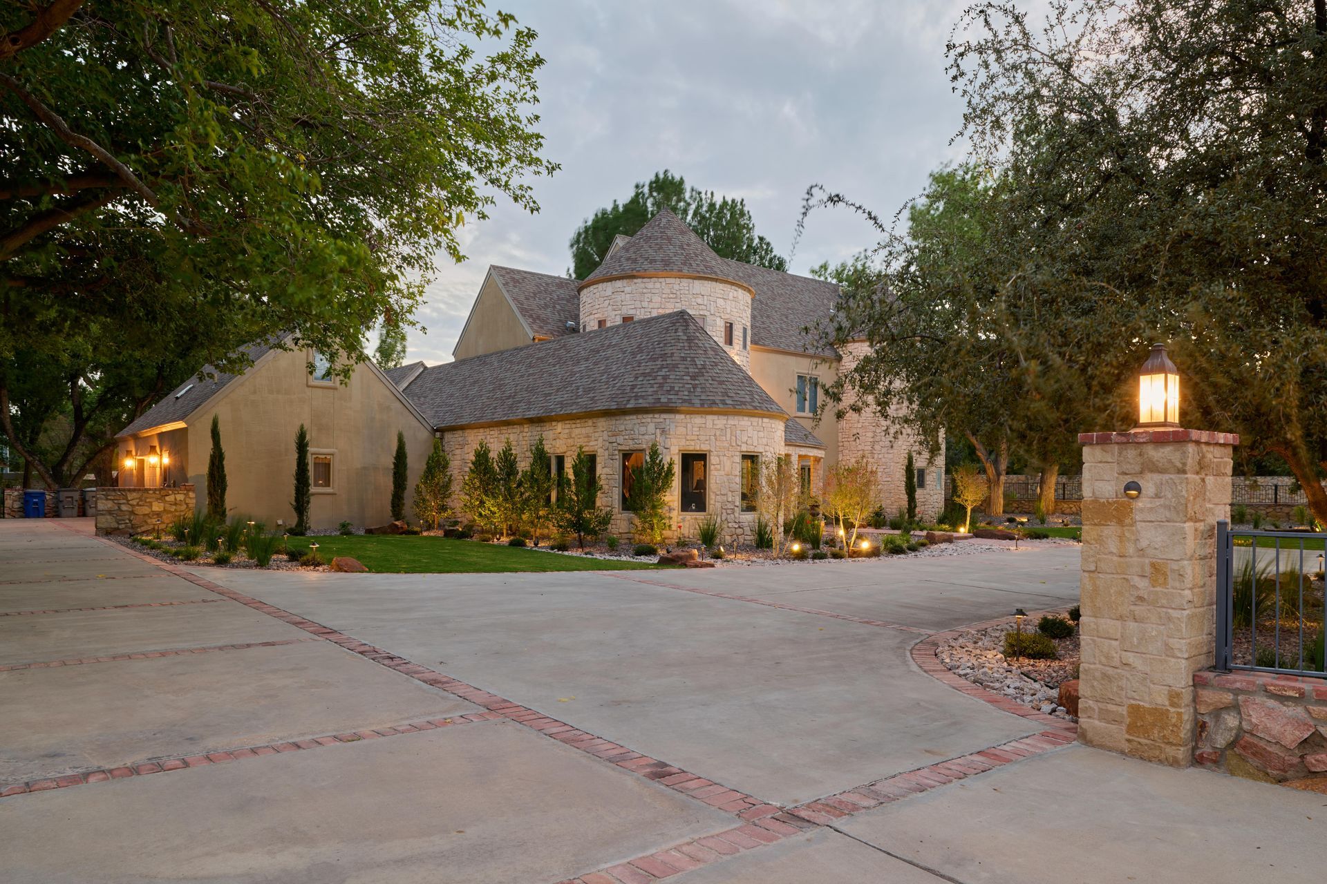 Large light-colored house with a circular turret, long driveway, and stone column with a lamp.