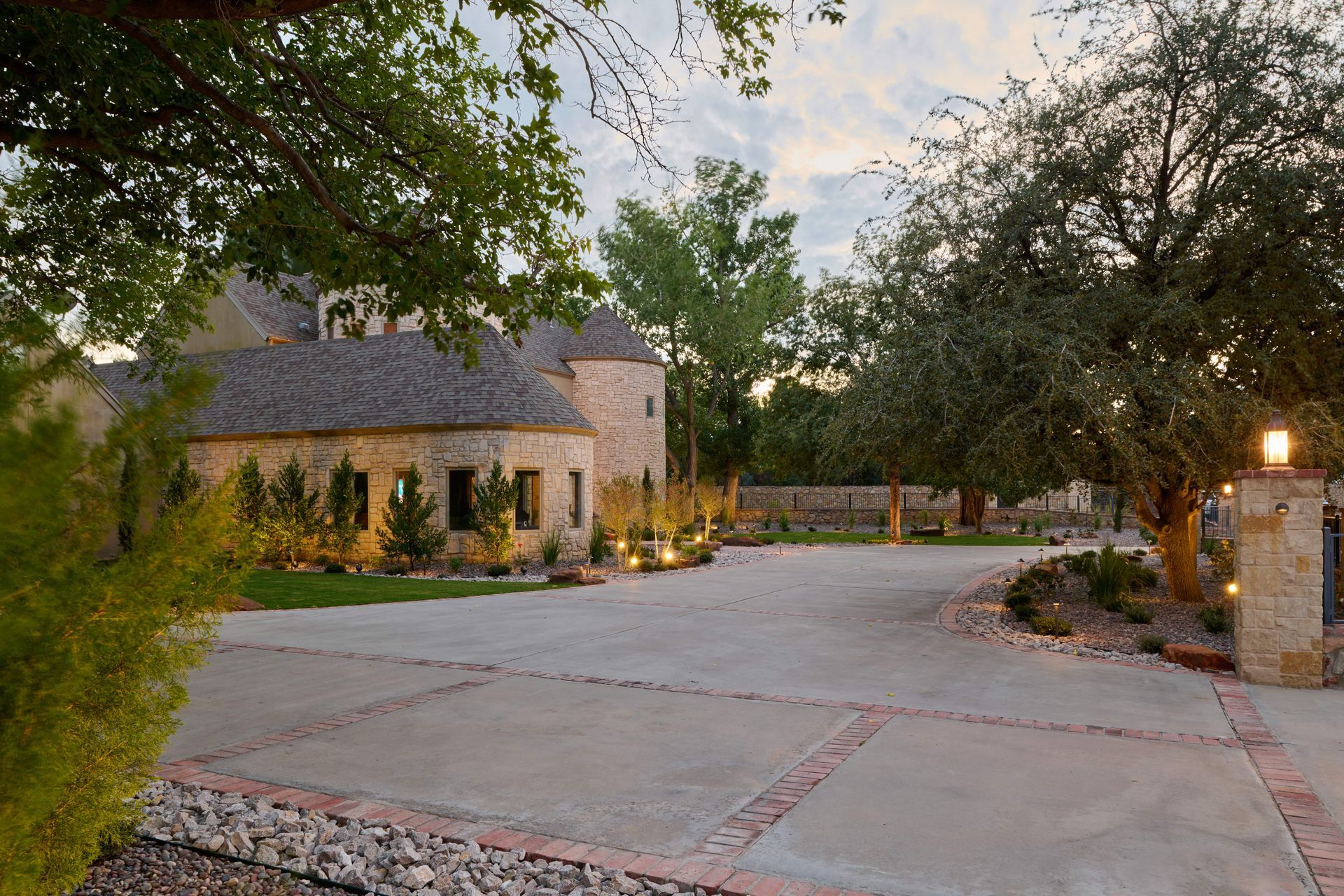 Stone house with circular turret and driveway lined with trees.