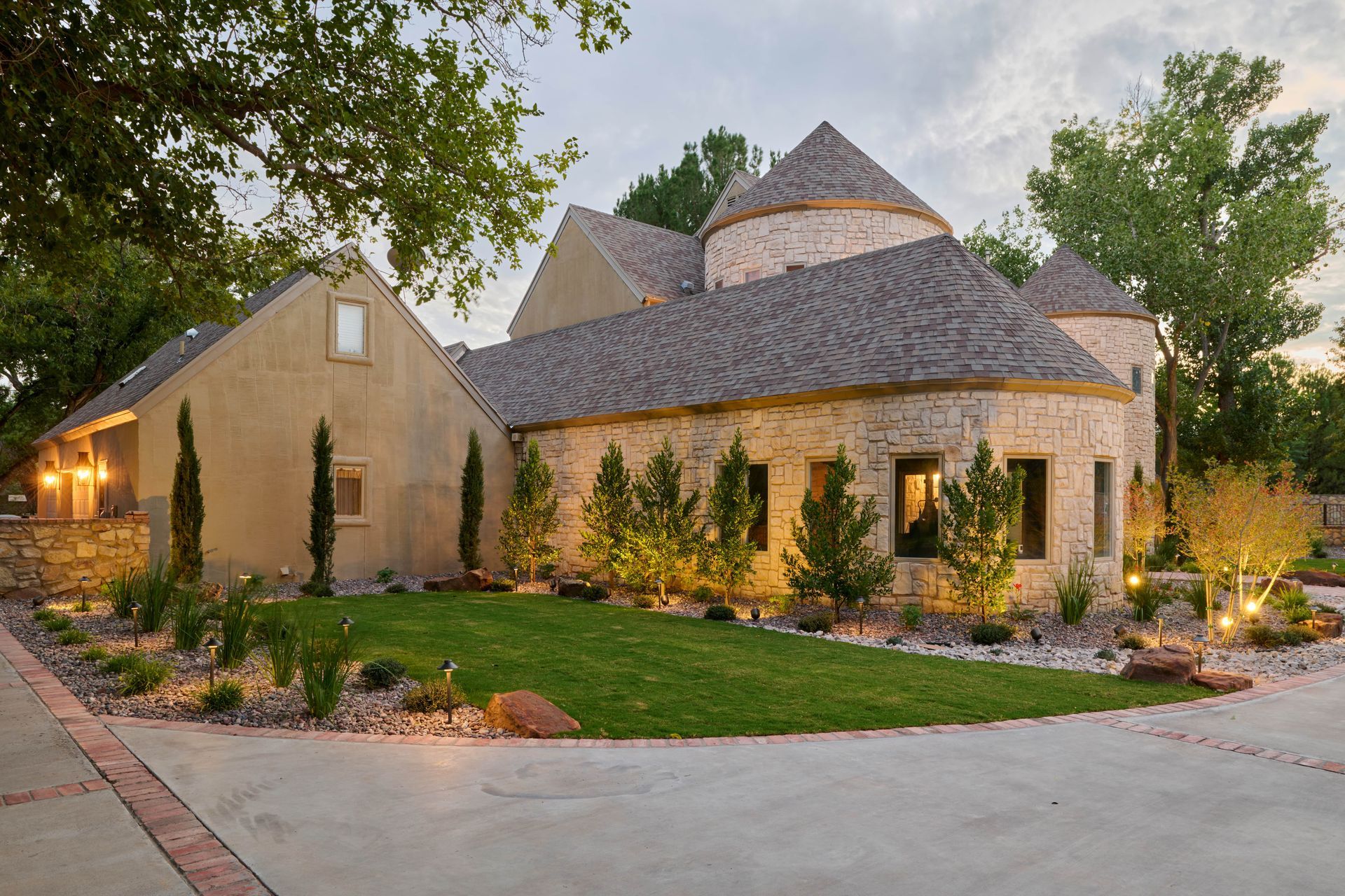 Stone house with rounded sections, brown roof, and manicured landscaping.