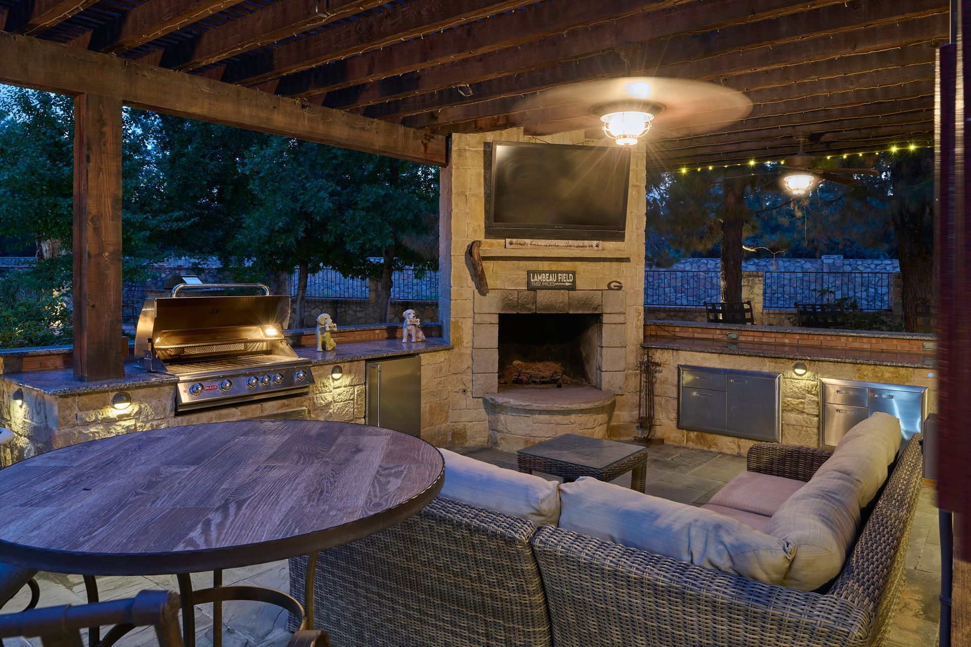 Outdoor patio with a stone fireplace, grill, seating, and a TV.