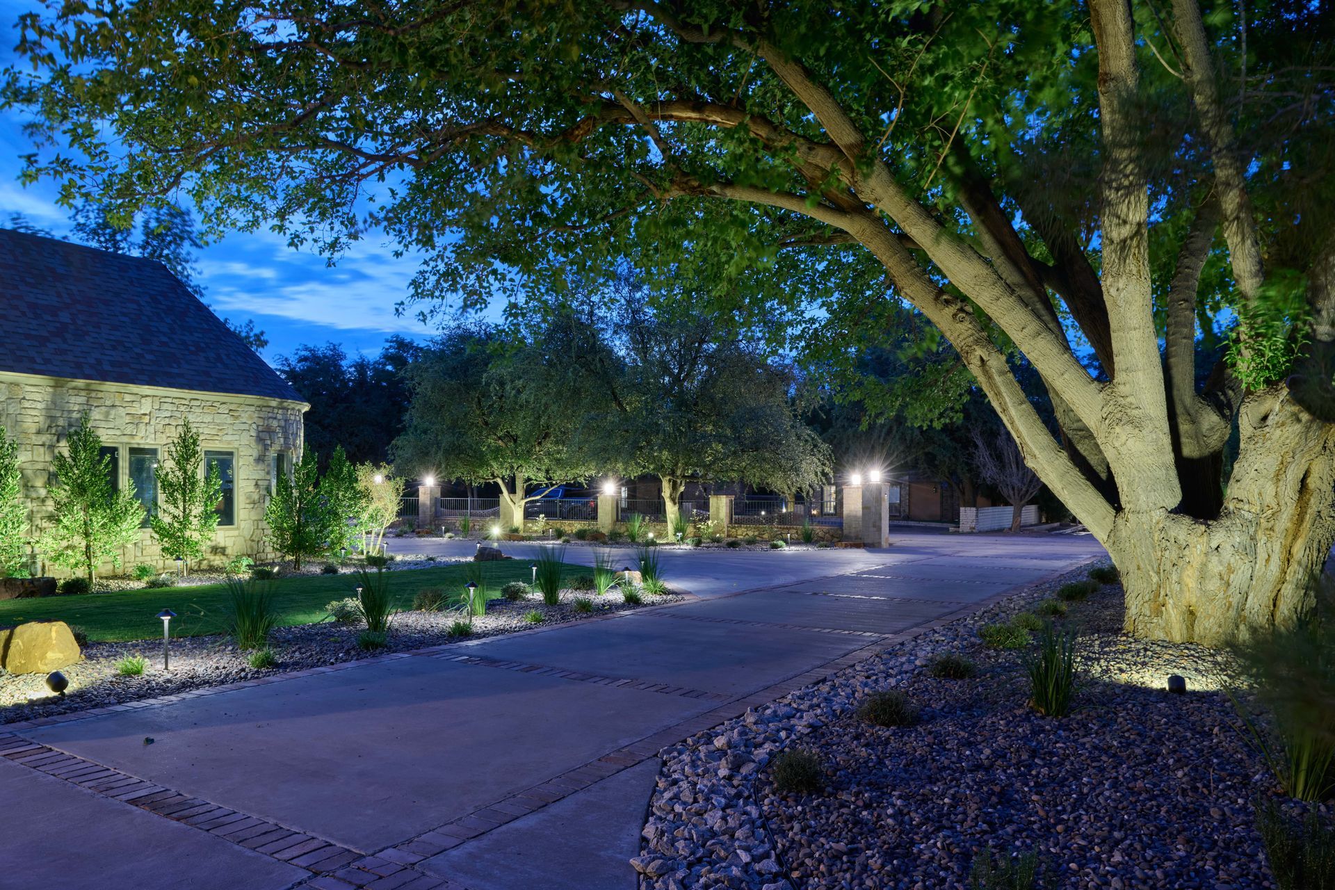 Night view of a house with a driveway lined with lights and trees.