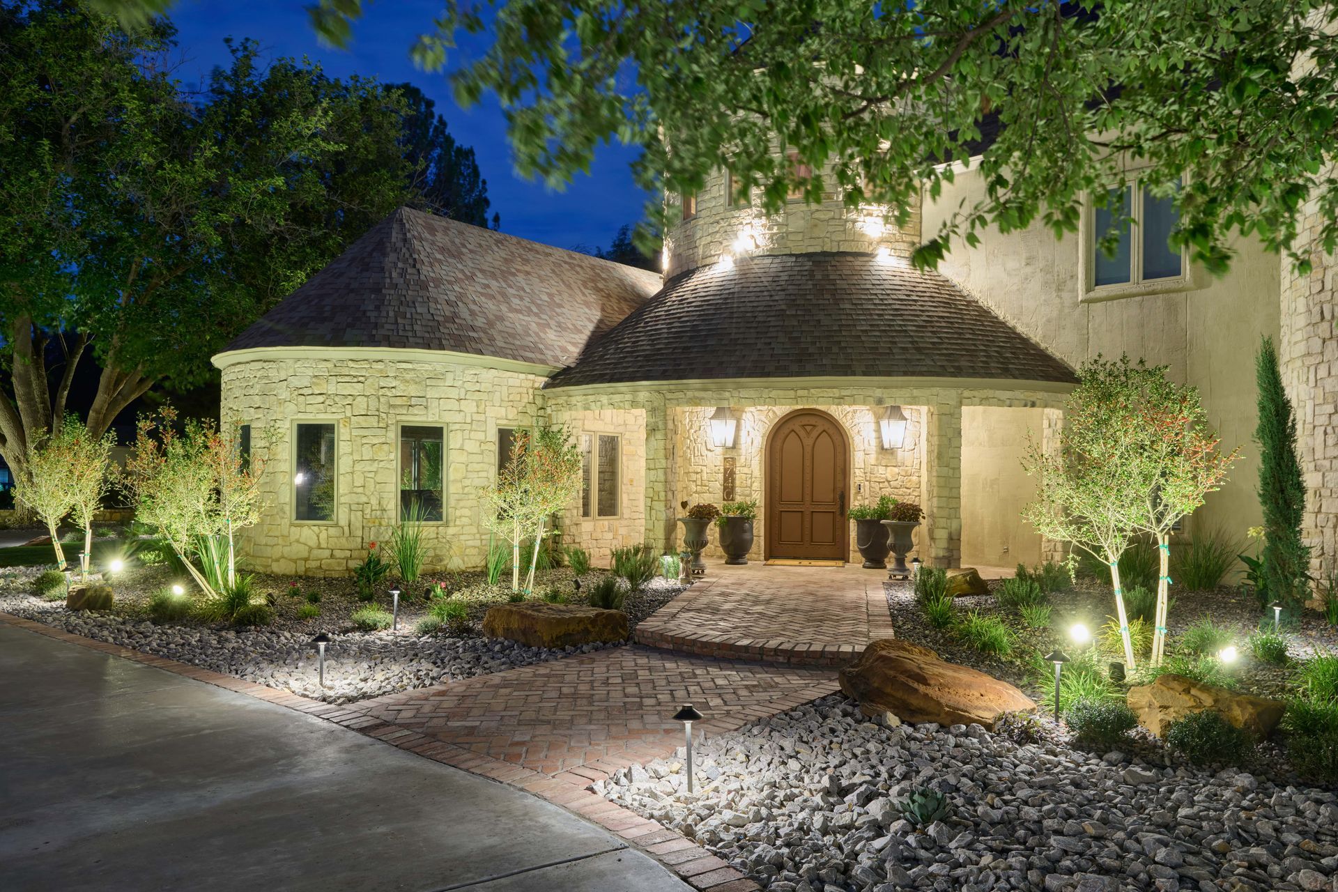 Night view of a house with landscape lighting illuminating the entrance, walkway, and trees.