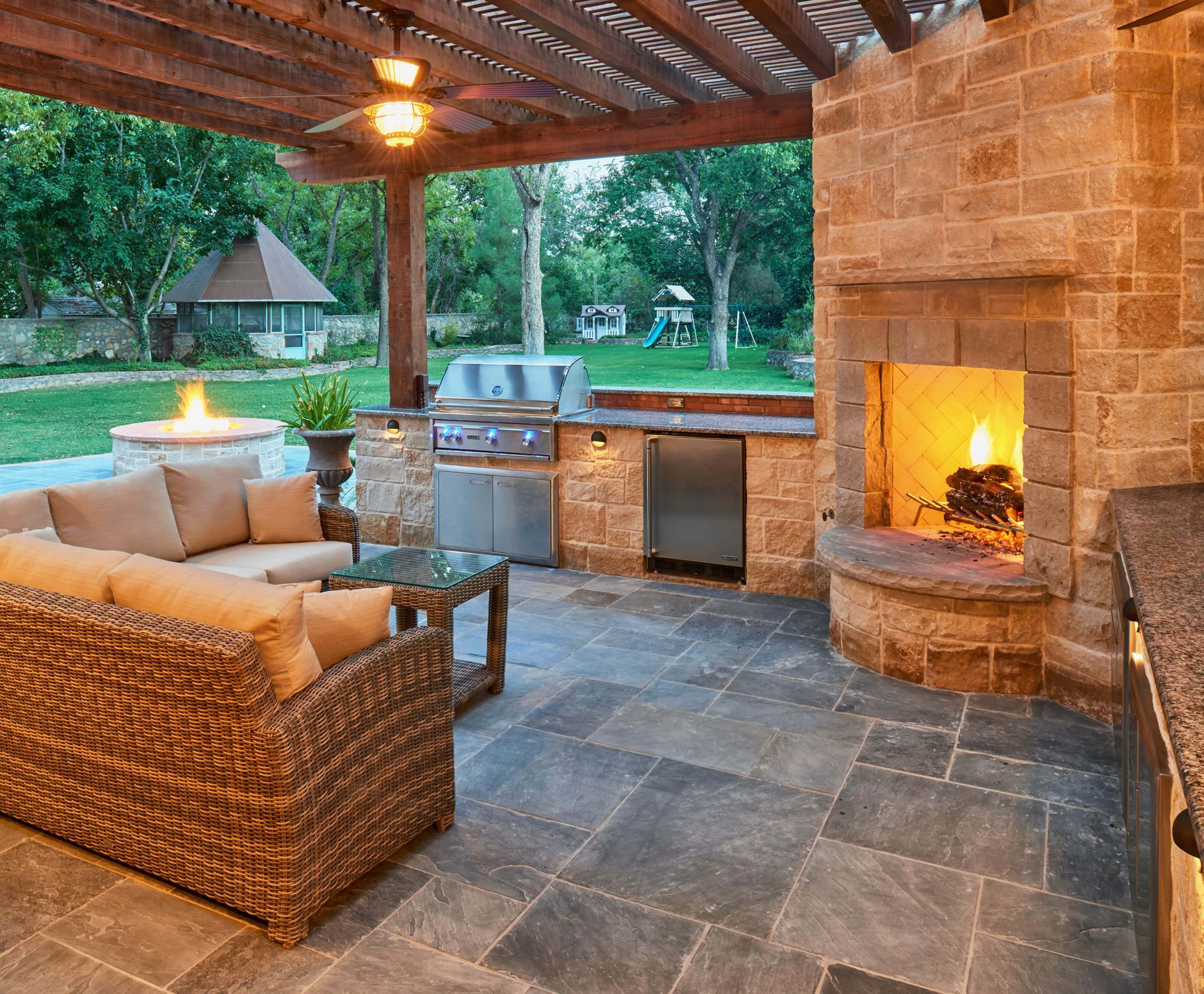 Outdoor patio with stone fireplace, grill, and seating under a wooden pergola.