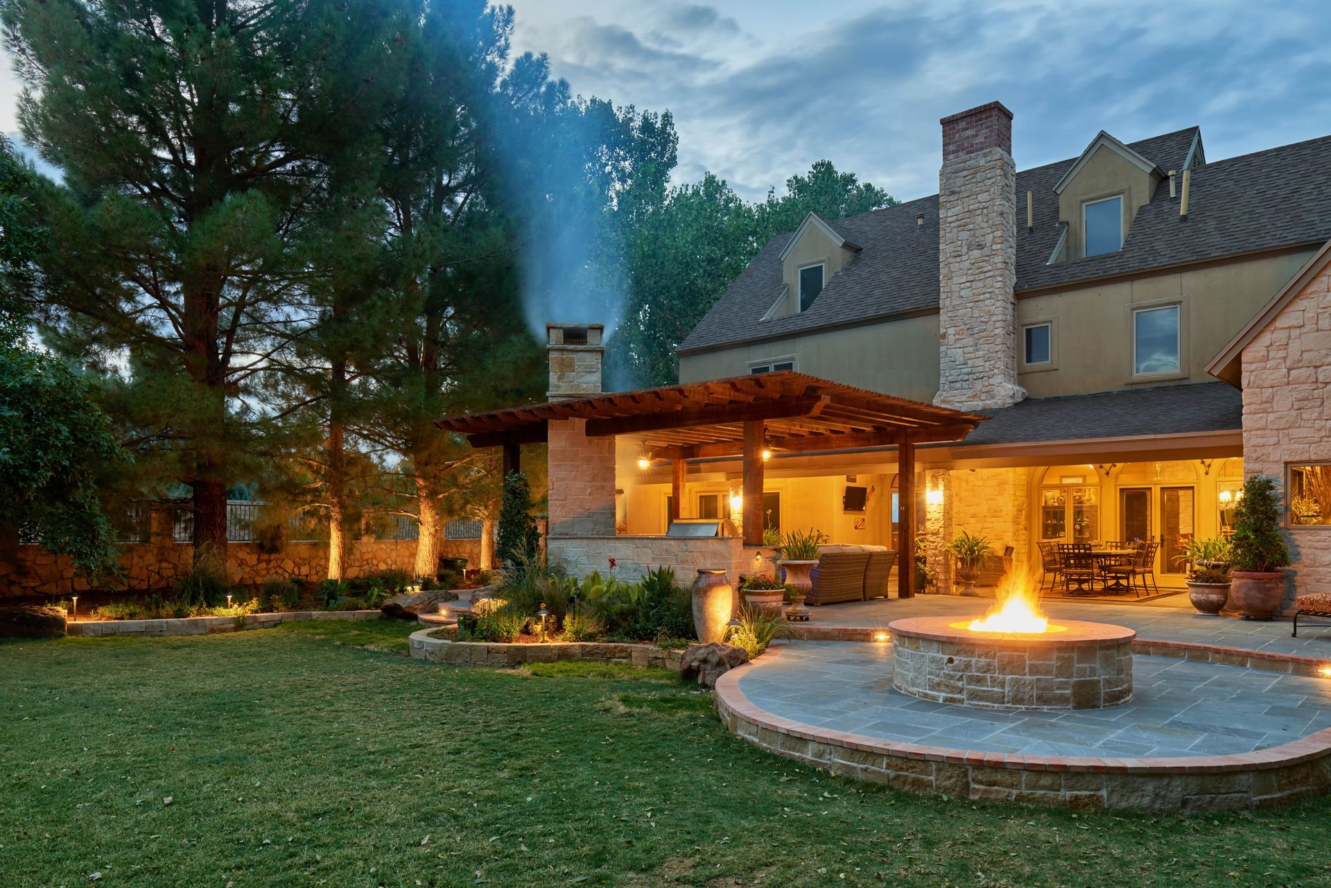 Backyard with illuminated fire pit, patio, and house at dusk.