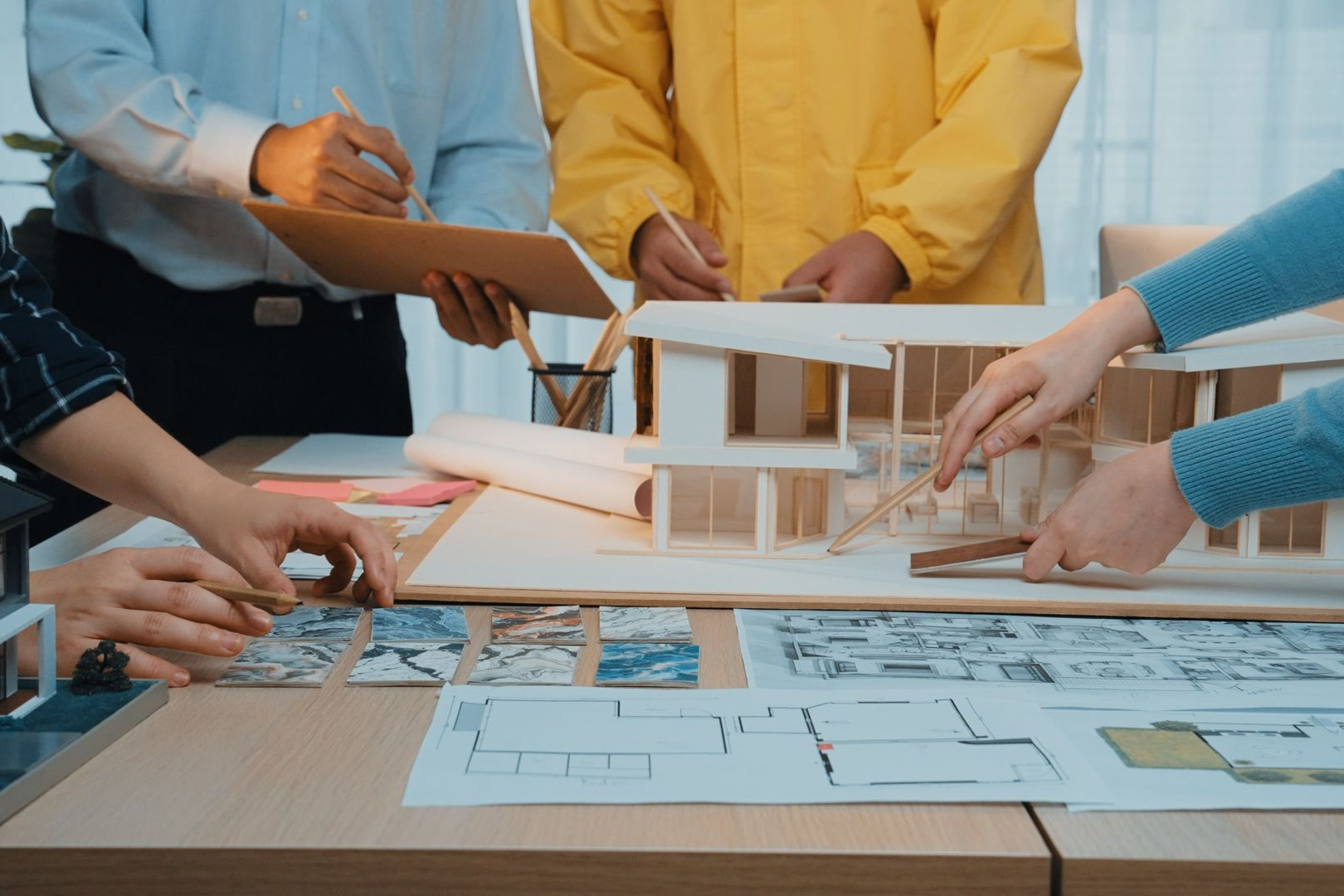 Architects collaborating around a model house, blueprints, and design plans.