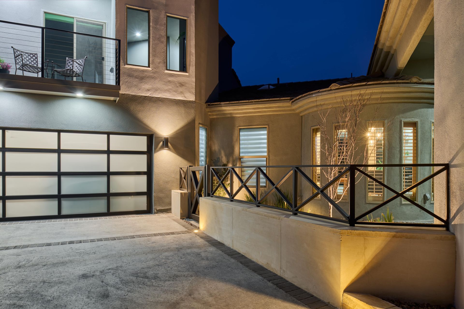 Modern home exterior at dusk, featuring a glass garage door and illuminated architectural details.