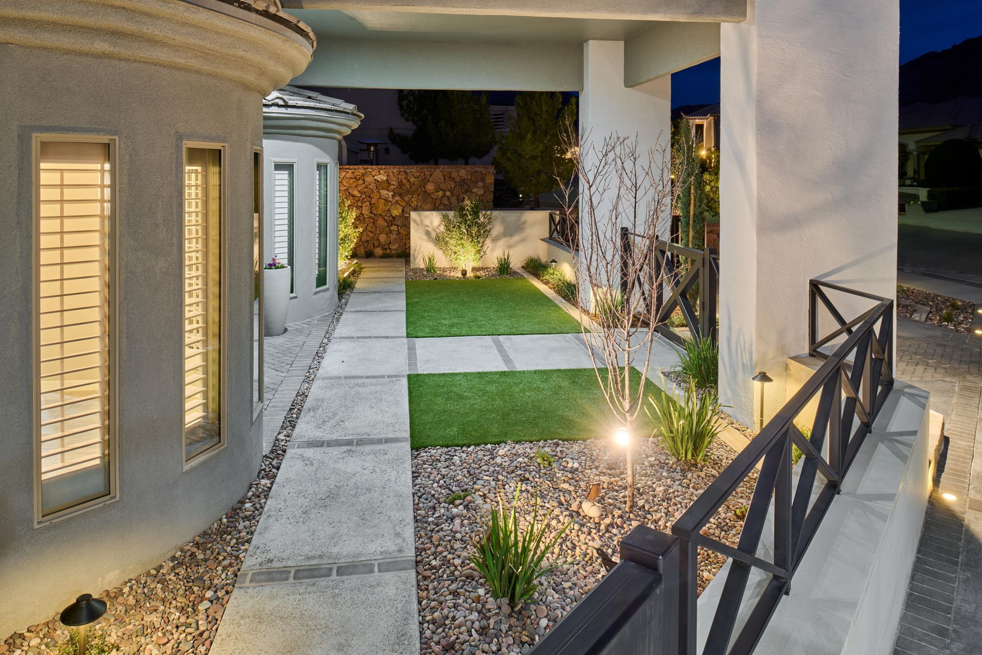 Exterior of a modern home with a walkway, grass, and decorative lighting.