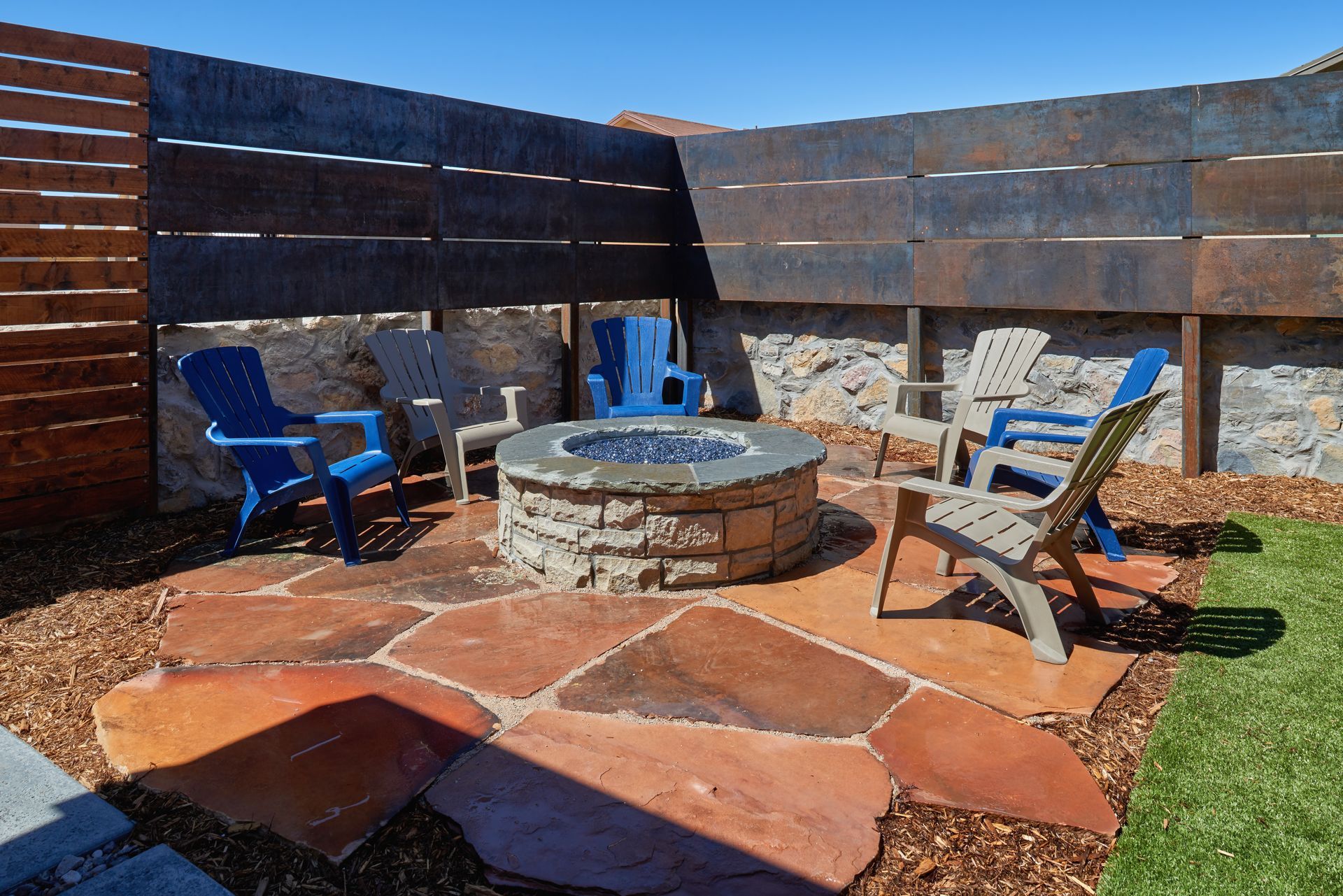 Fire pit area with stone patio, surrounded by chairs and a rusty metal fence.